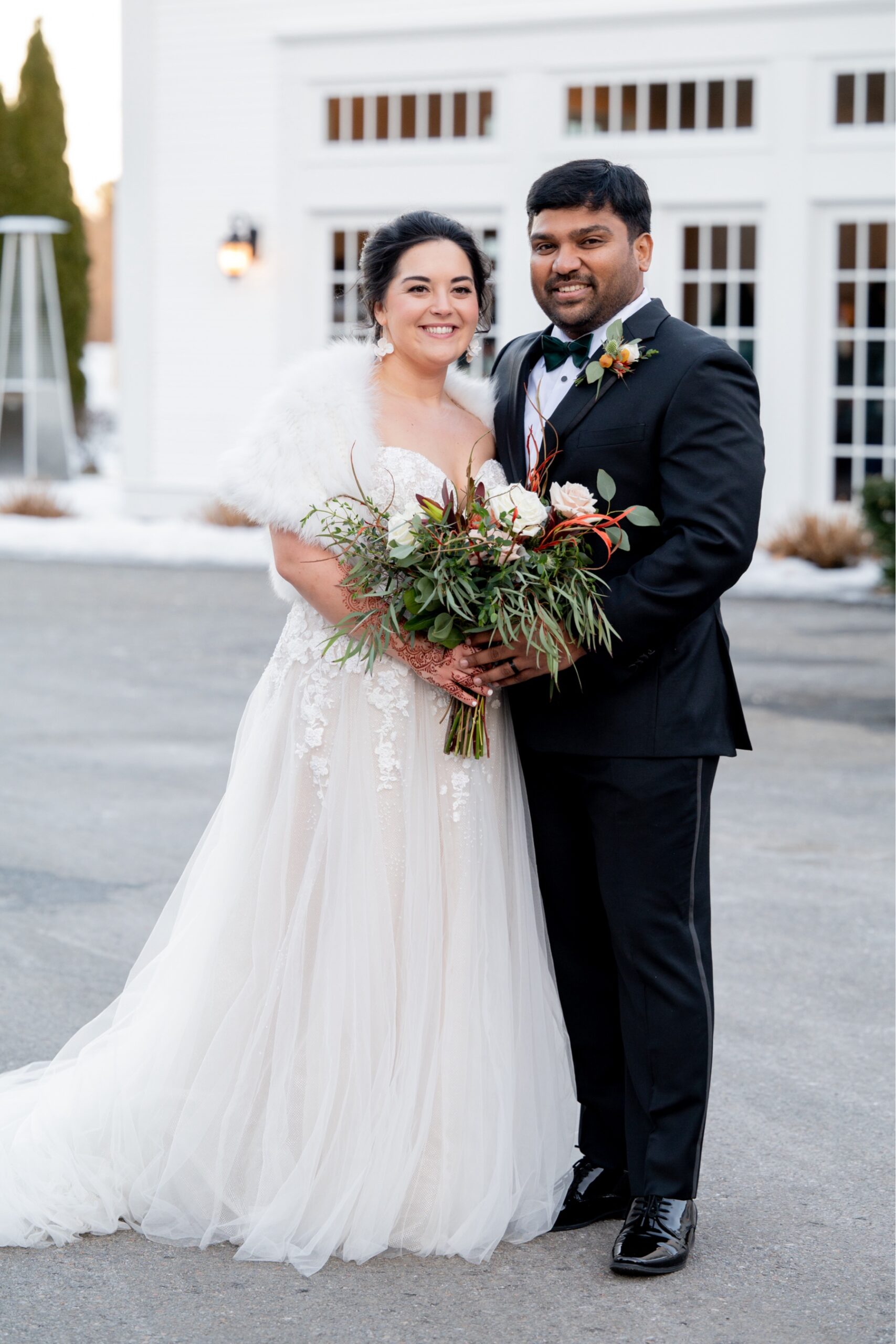 bride and groom smiling at camera as bride holds green filled bouquet 