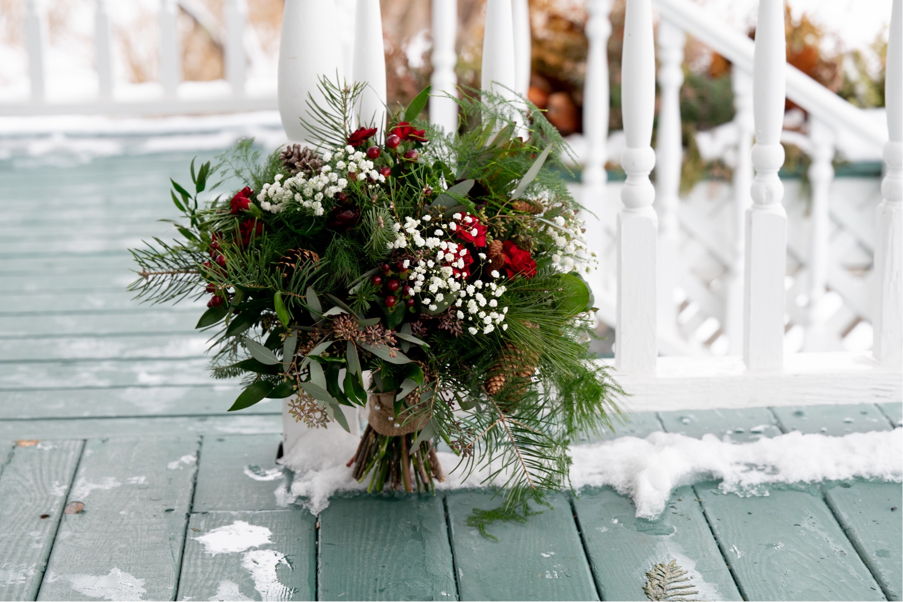 wedding bouquet of white and red flowers and extra greenery and pine cones 