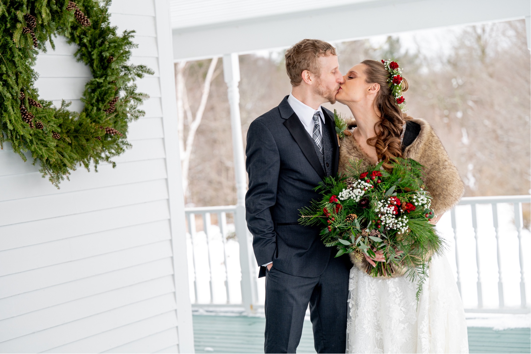 bride and groom kissing on porch with christmas wreath on wall for a Winter Wonderland Wedding