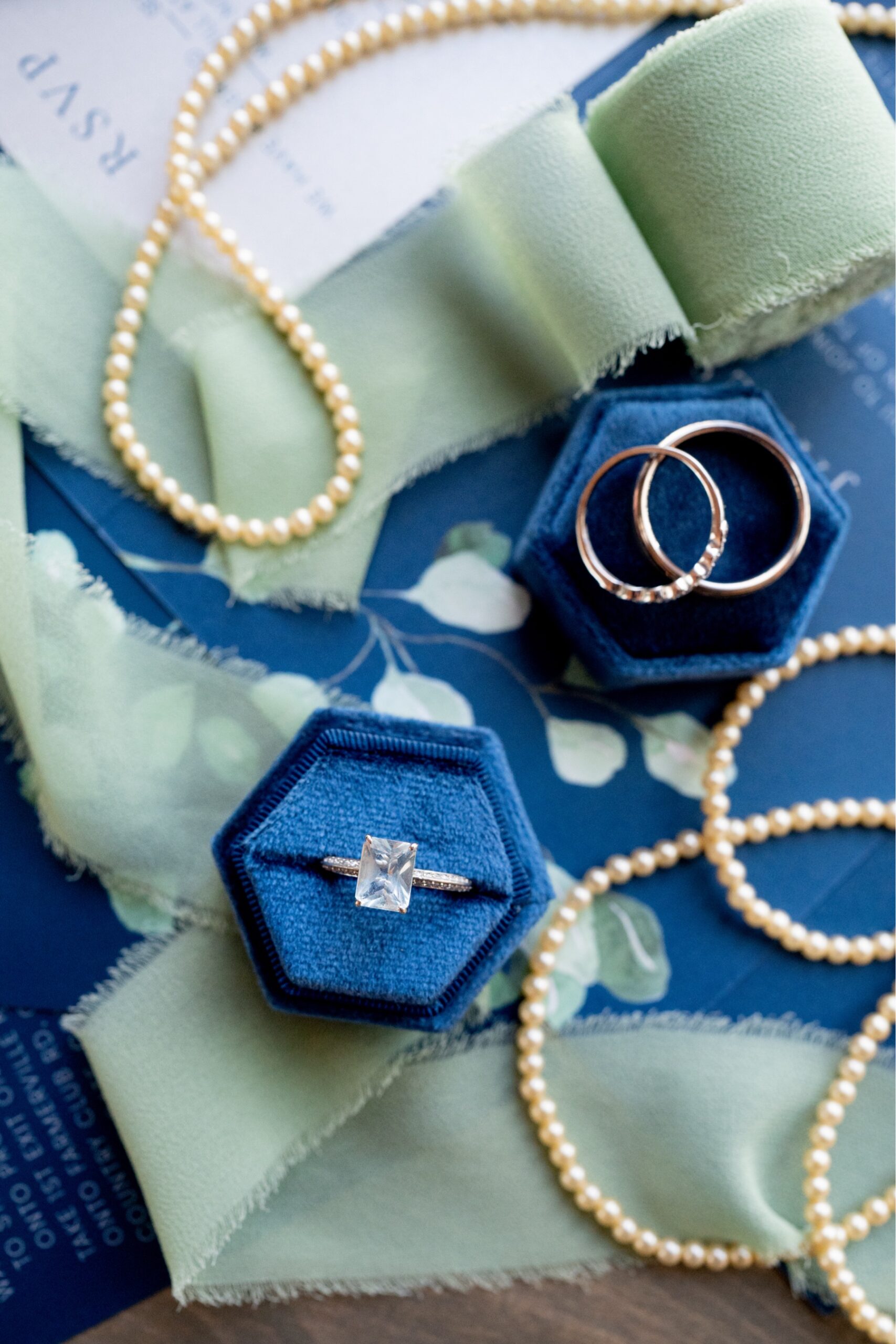 wedding rings and pearls sitting on top of blue stationary and green ribbons for a Winter Wonderland Wedding