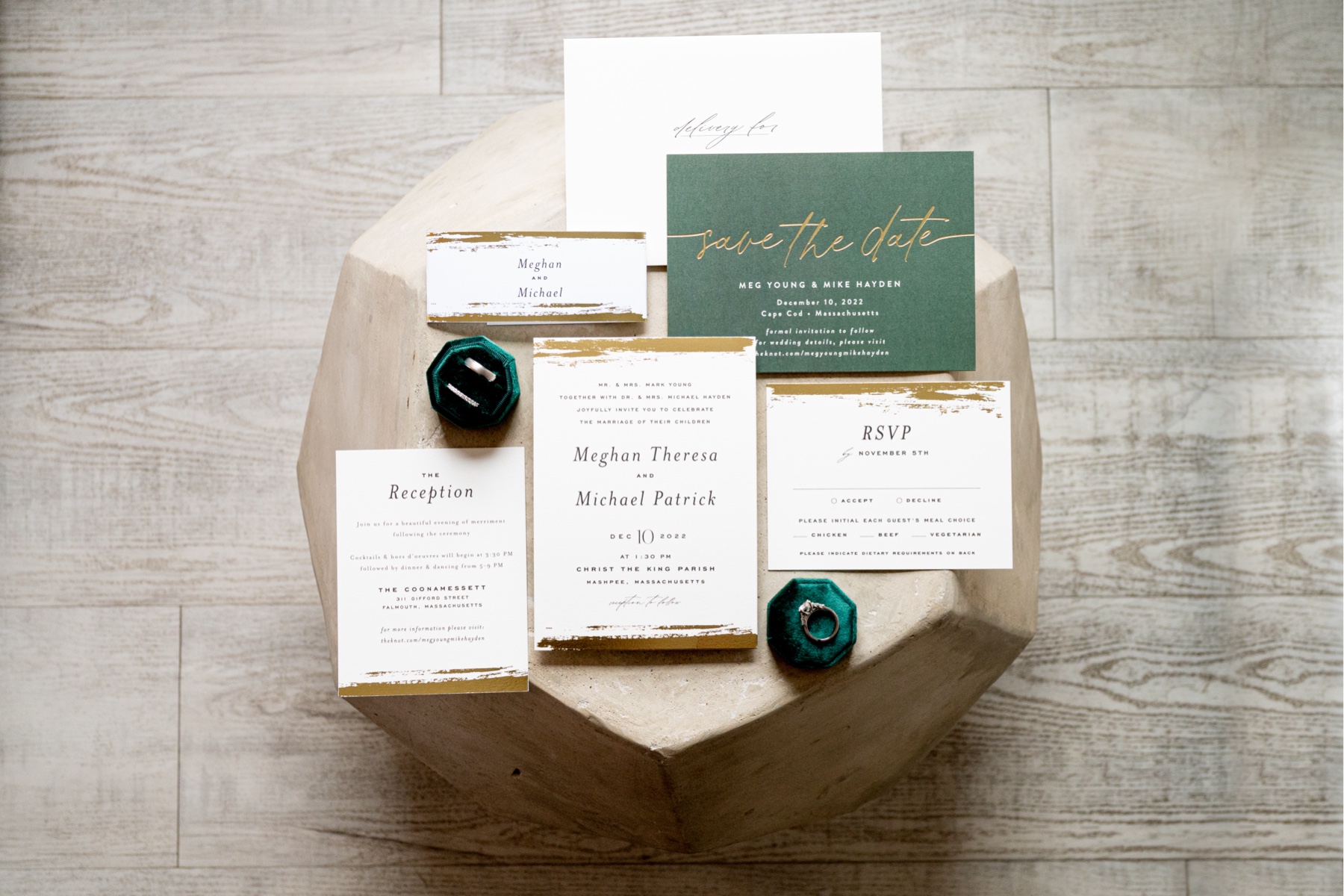 white and gold and green wedding invitations situated on a table with wedding rings in green ring boxes