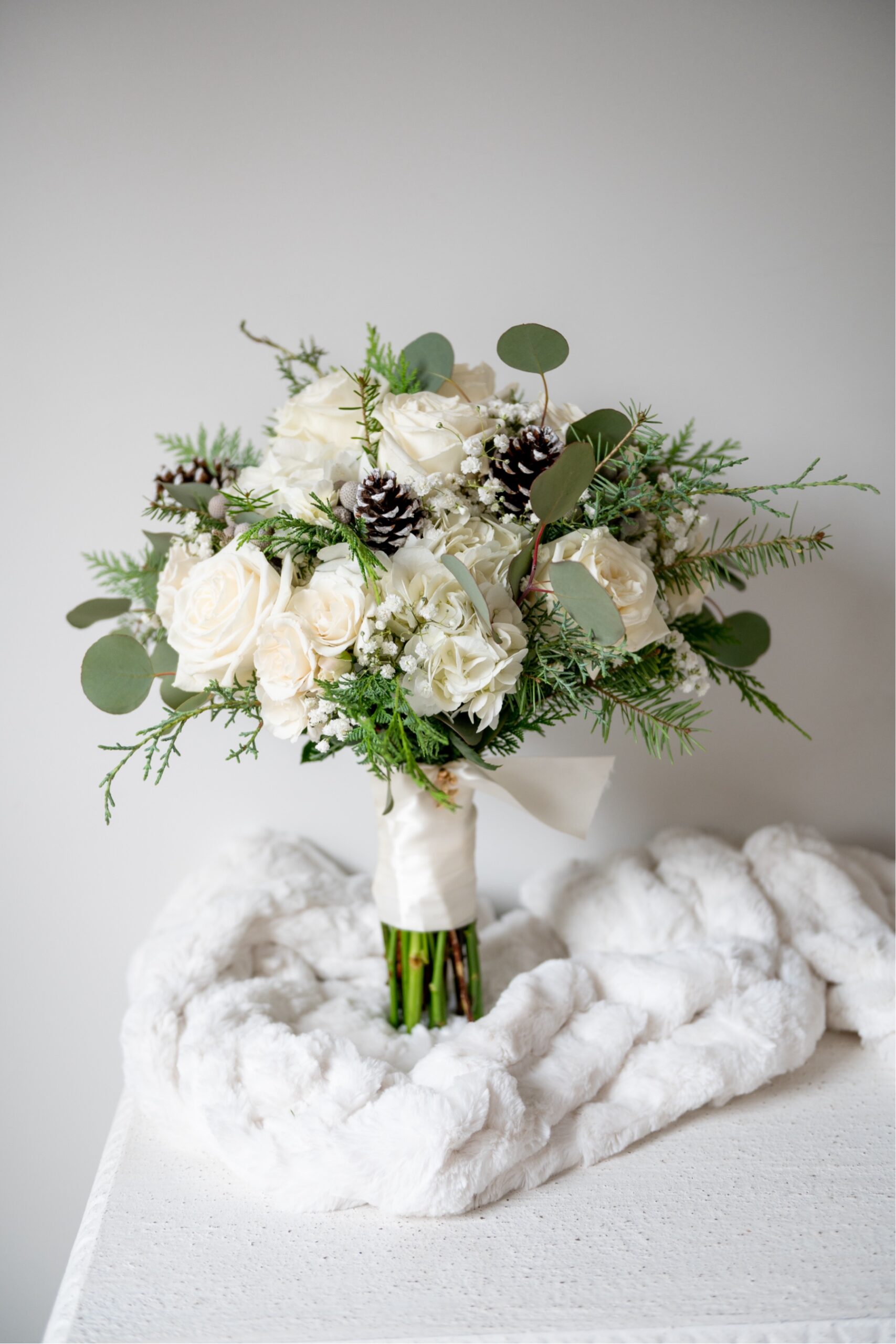 wedding bouquet of white flowers, greenery and snow dusted pine cones 