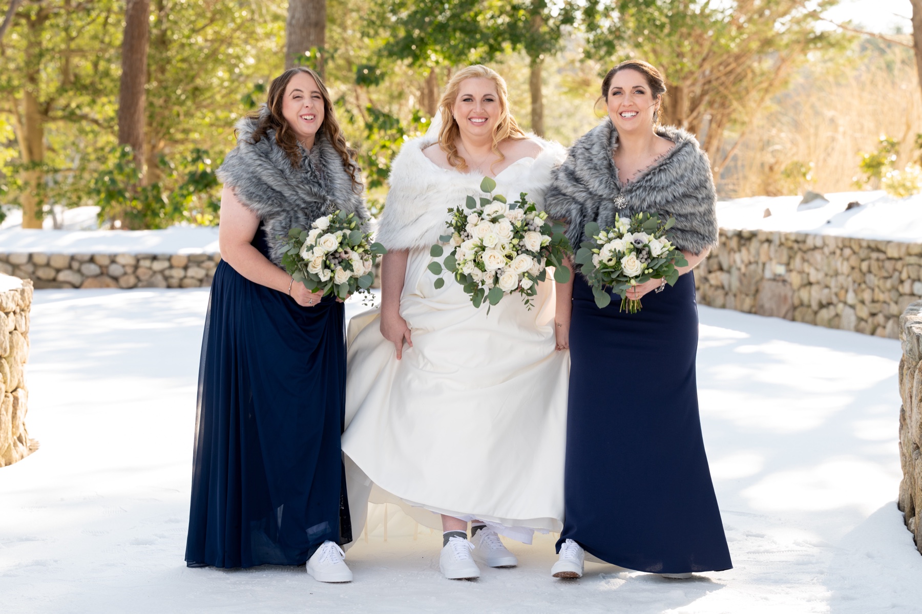 bride standing with bridesmaids who are wearing navy dresses and grey shawls surrounded by snow at a Winter Wonderland Wedding