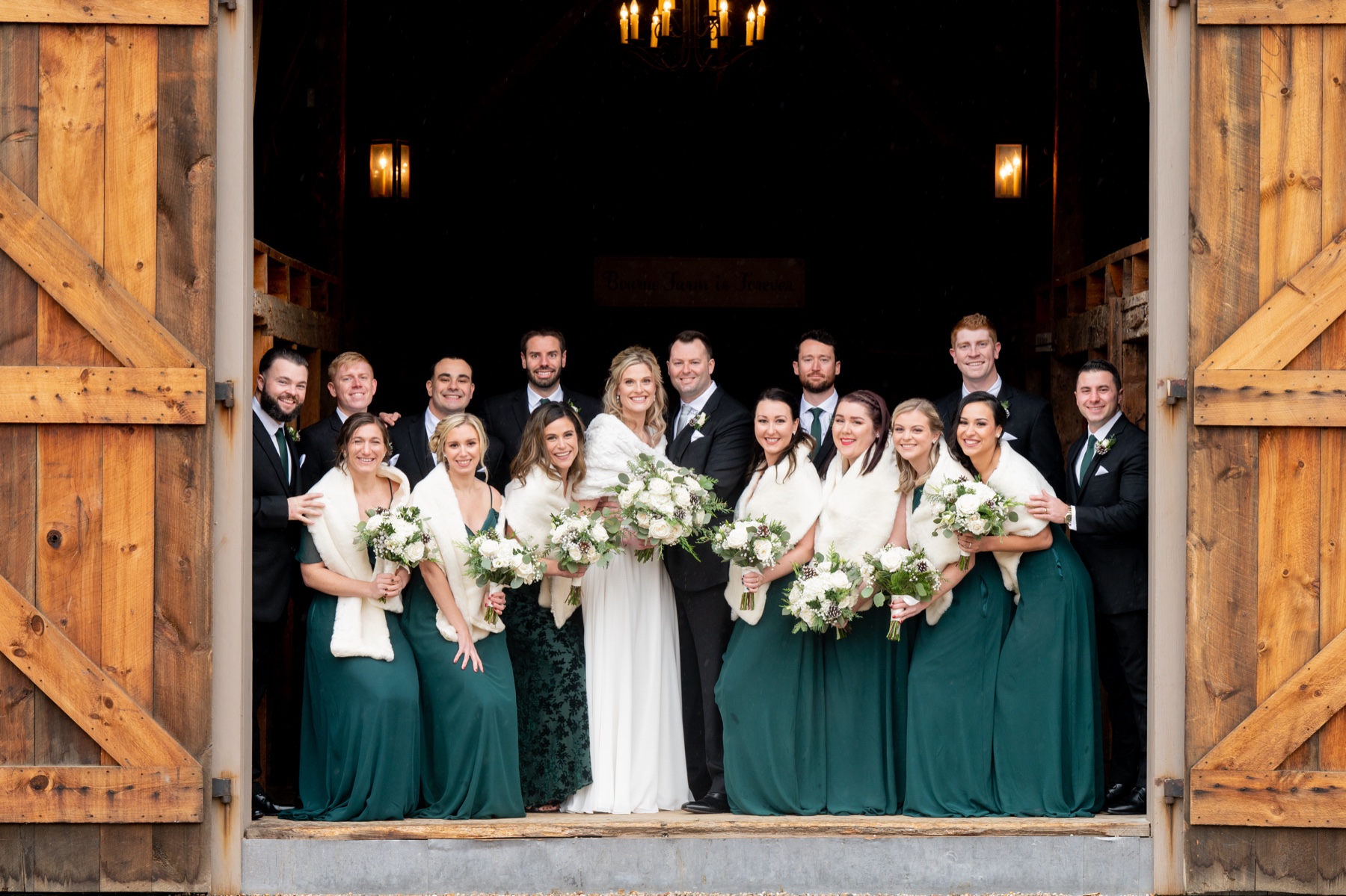 bride and groom standing with wedding party in front doorway of wood barn