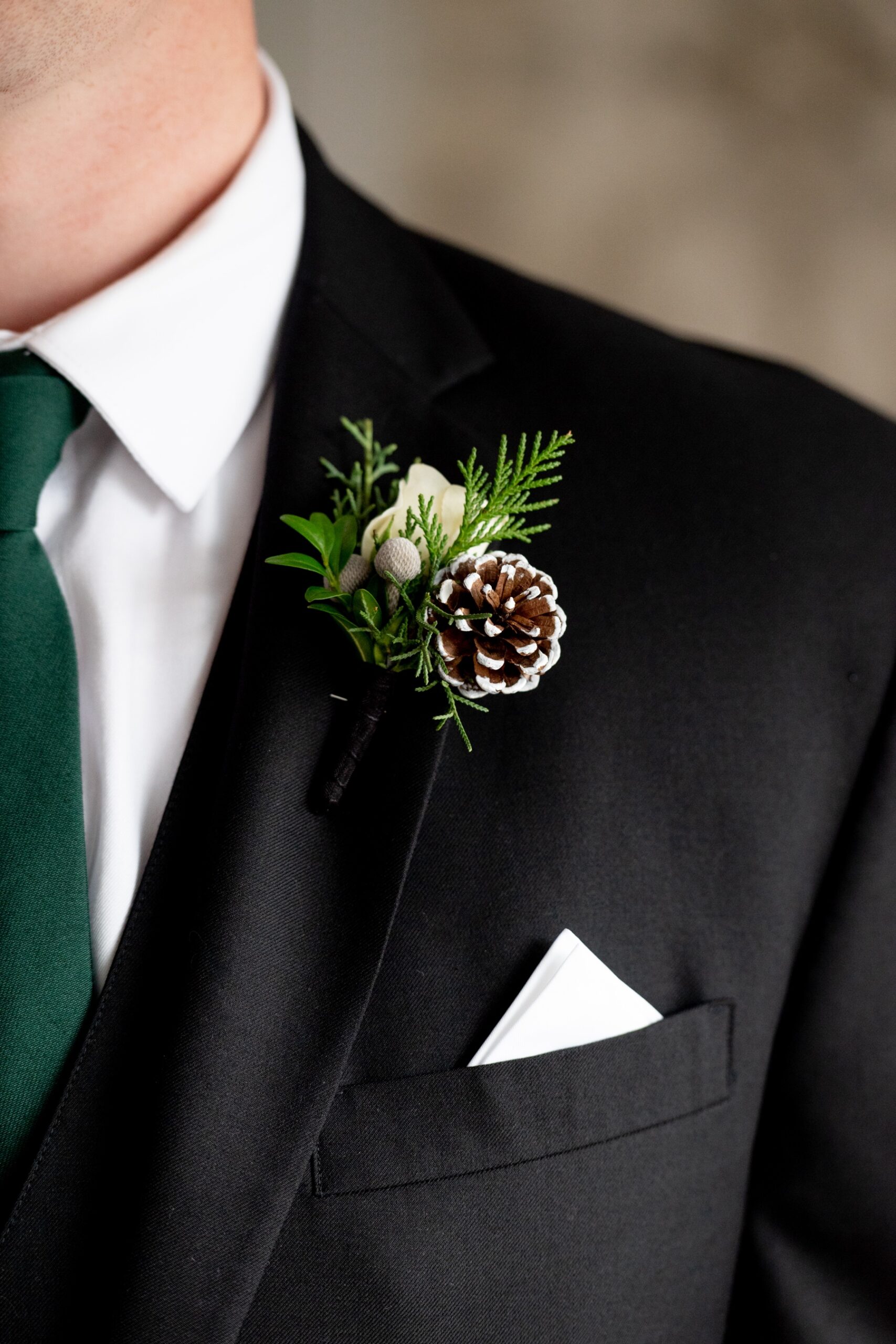 close up of groom's wedding bouquet of snow dusted pine cone and greenery 