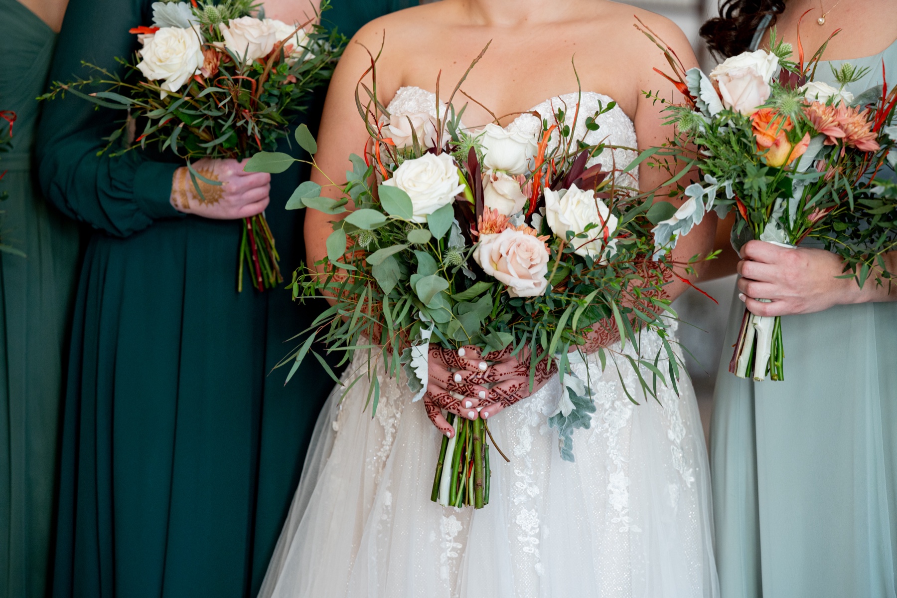 bride and bridesmaids holding wedding bouquets of white and pink and orange flowers and greenery 