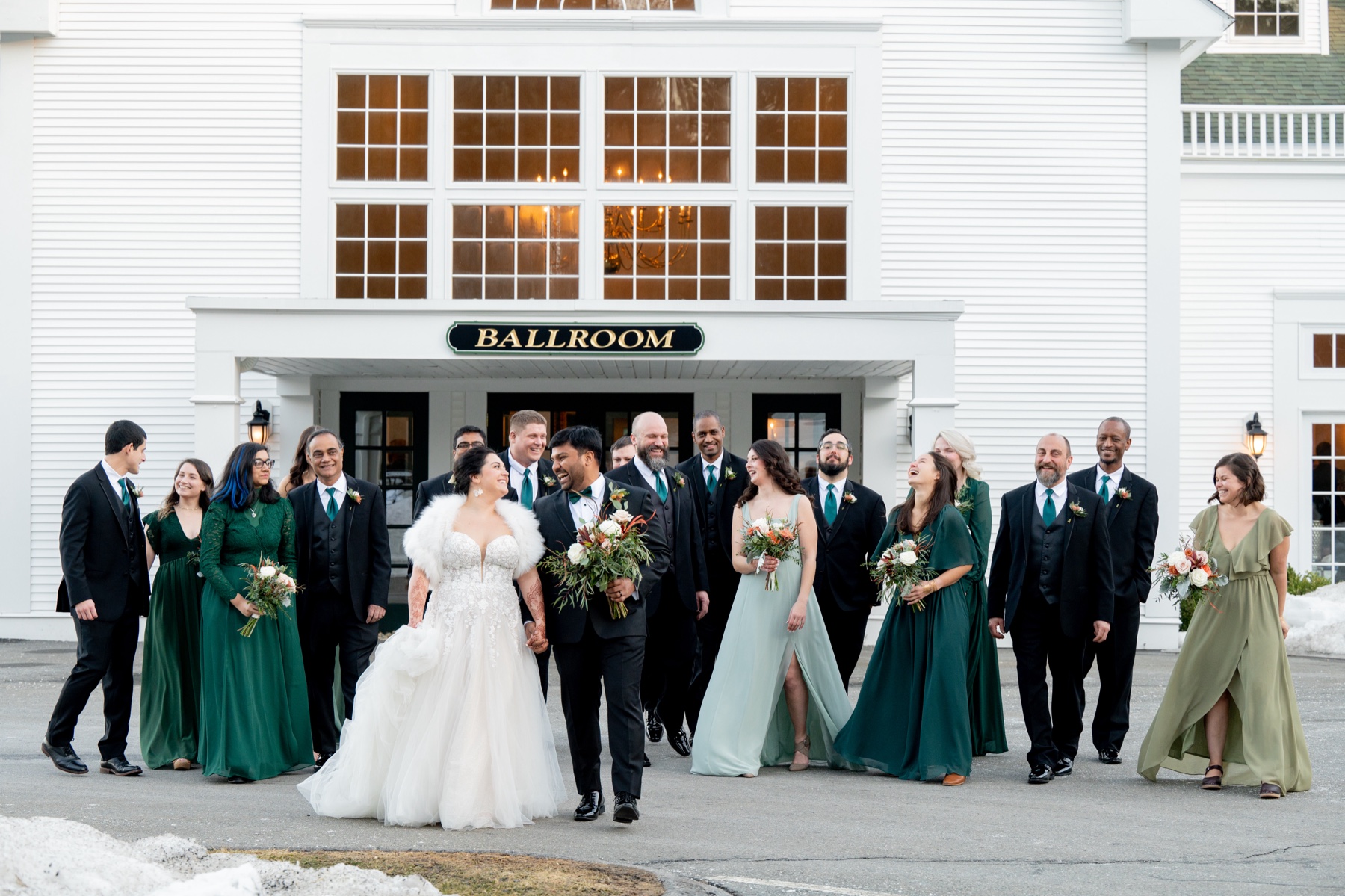 bride and groom walking in front of the building with bridesmaids in green dresses and groomsmen in black suits behind them