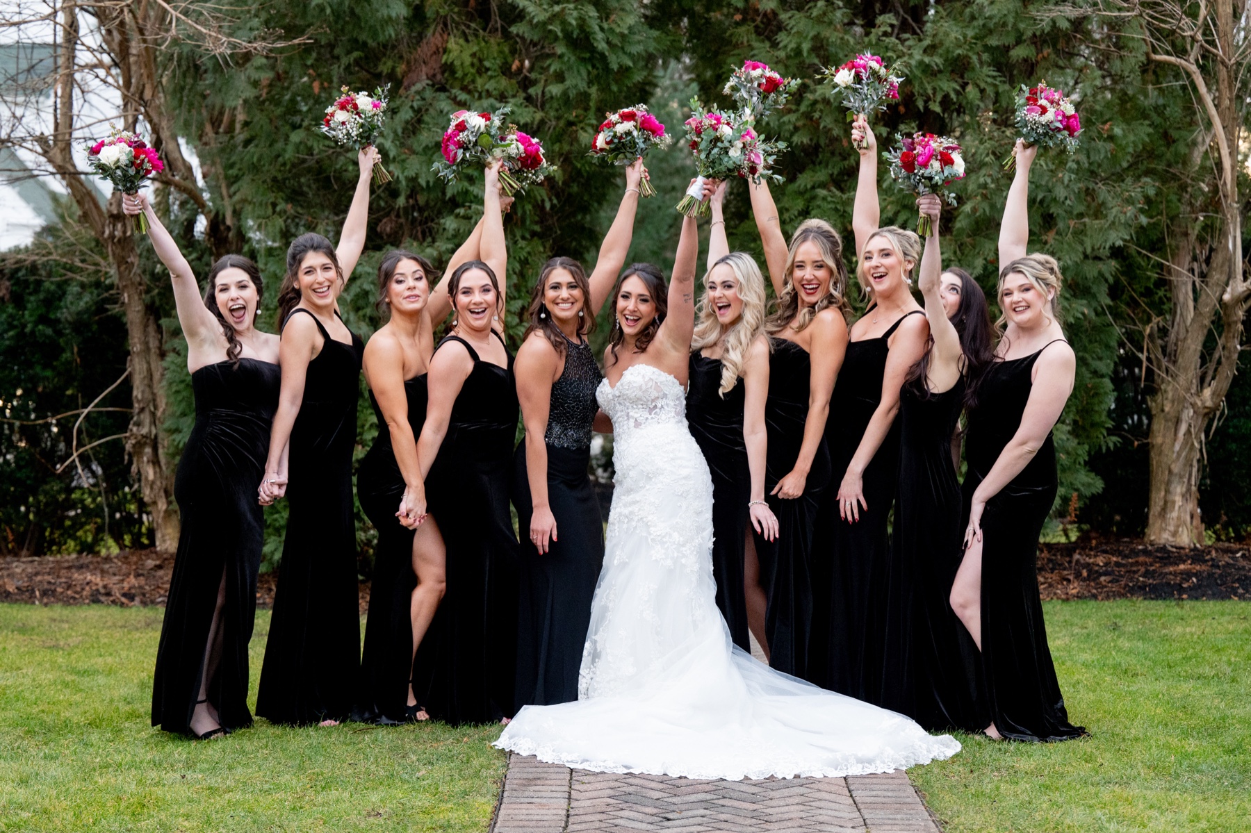 bride standing with bridesmaids in black dresses holding pink and green wedding bouquets overhead 