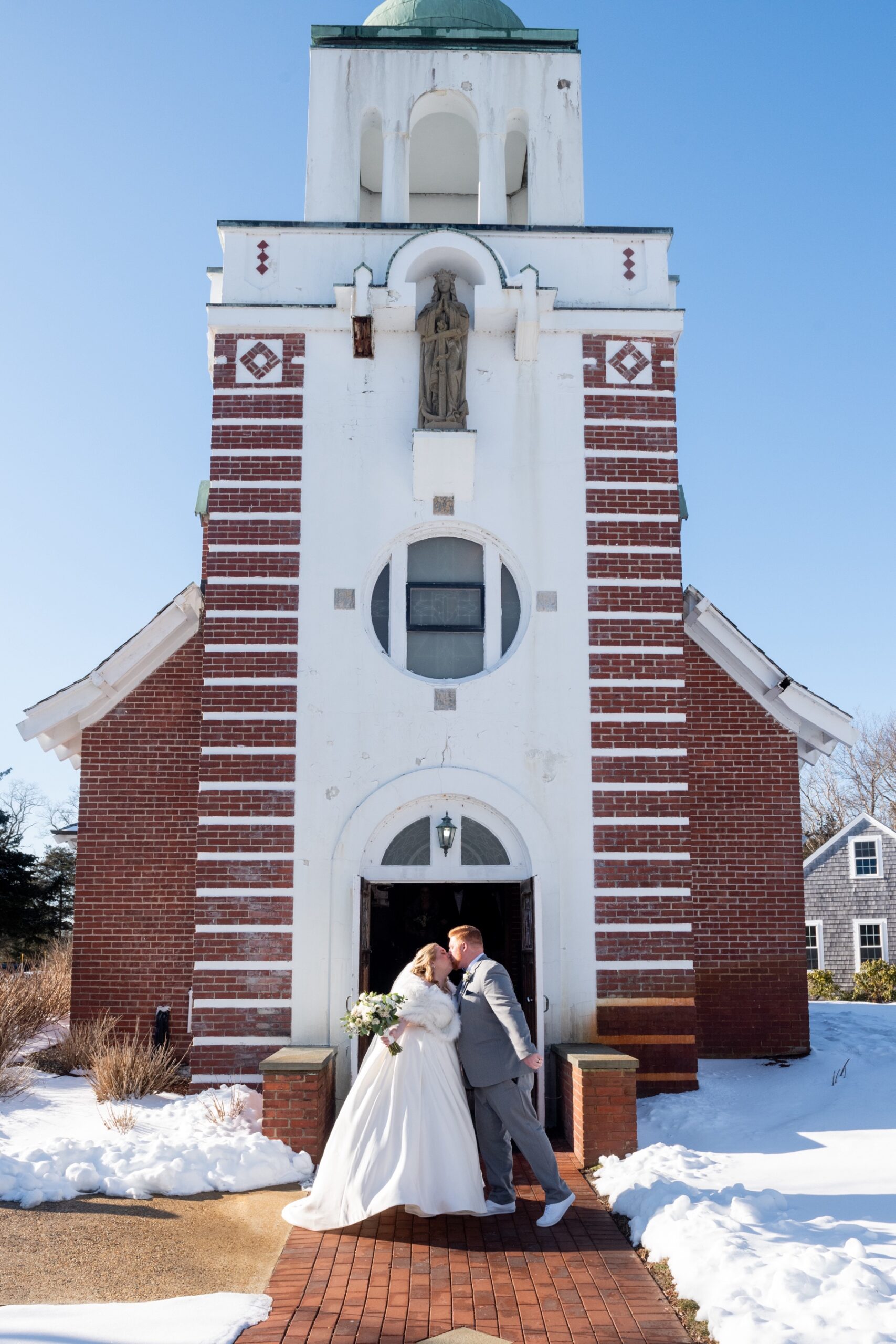 bride and groom kissing in front of church surrounded by snow at their Winter Wonderland Wedding