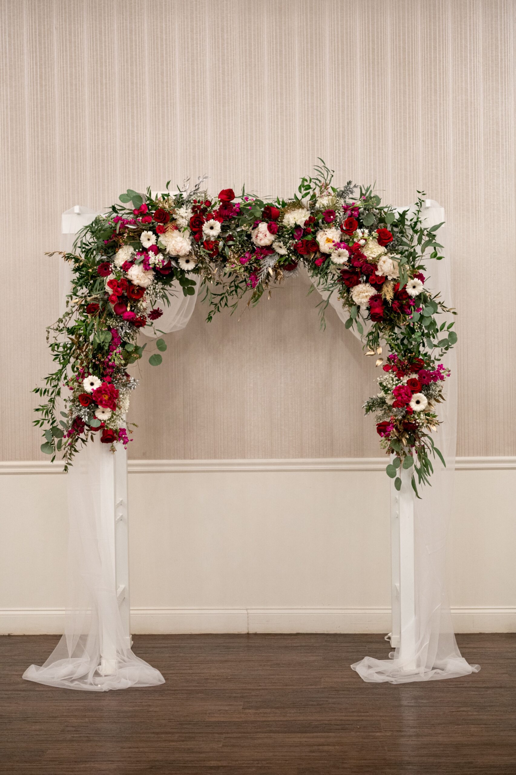 white wedding arch filled with red and white flowers and greenery 