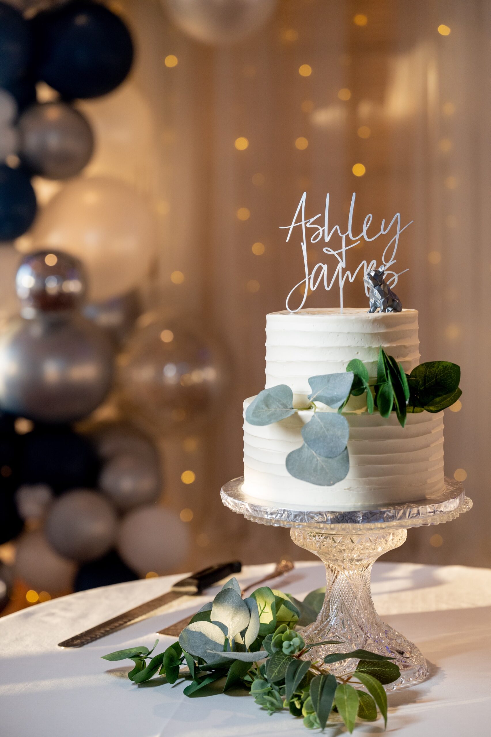 white wedding cake with greenery and a dog figurine as a cake topper 