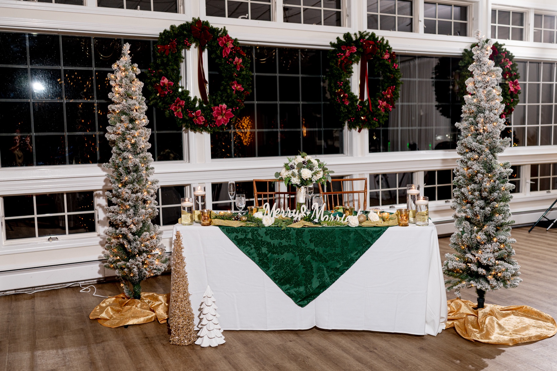 christmas decor at wedding reception with christmas trees and christmas wreaths and green and white tables