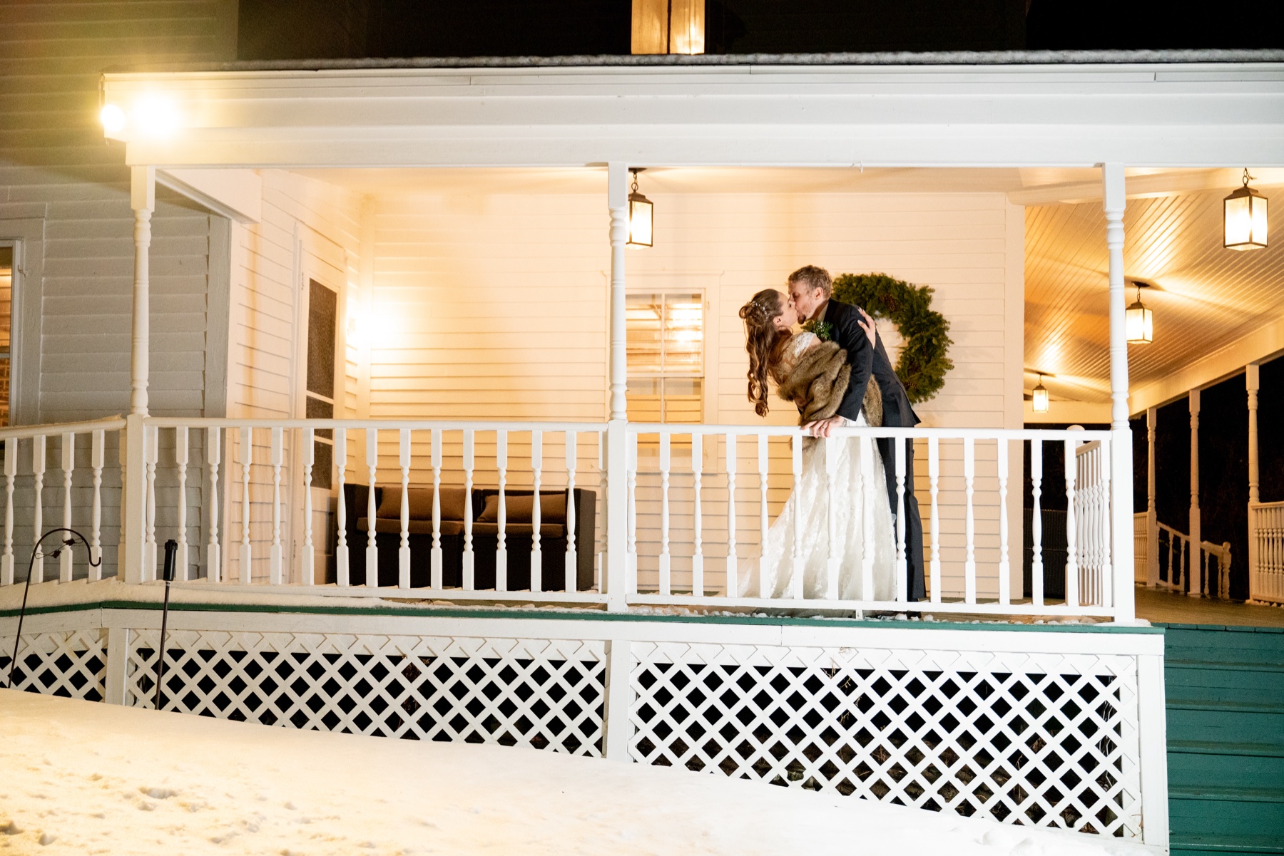 bride and groom kissing on front porch of wedding reception with christmas wreath behind them