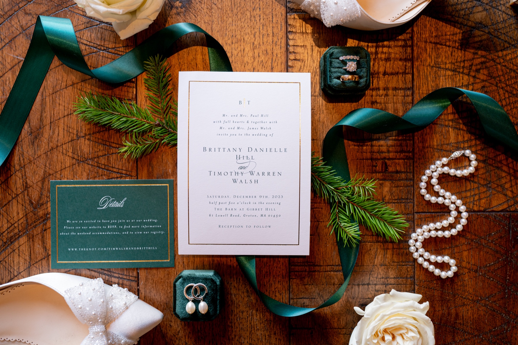 a Winter Wonderland Wedding flatlay of white and green invitations, pearl necklace, white bridal shoes and white flowers 