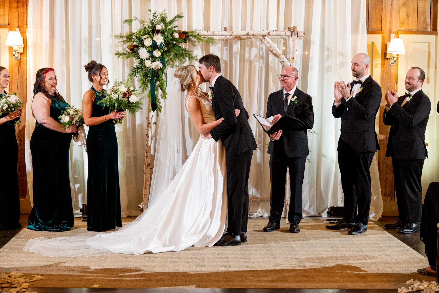 bride and groom kissing at the end of their Winter Wonderland Wedding ceremony indoors as guest clap and smile