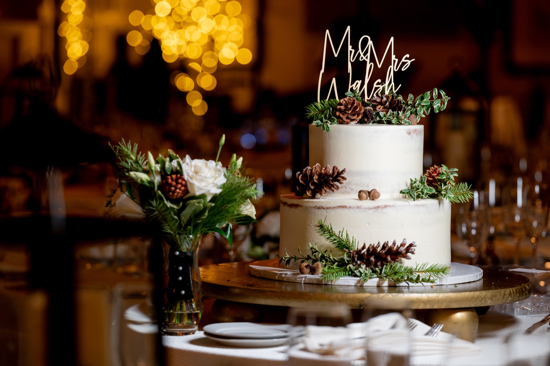 a Winter Wonderland Wedding cake decorated with white frosting, greenery and pine cones 