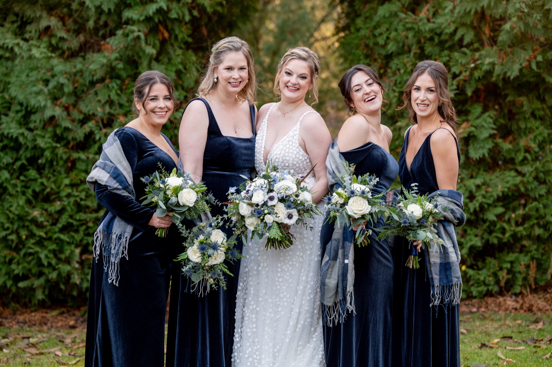 bride standing with her bridesmaids wearing blue velvet Winter Wonderland Wedding dresses and blue shawls 