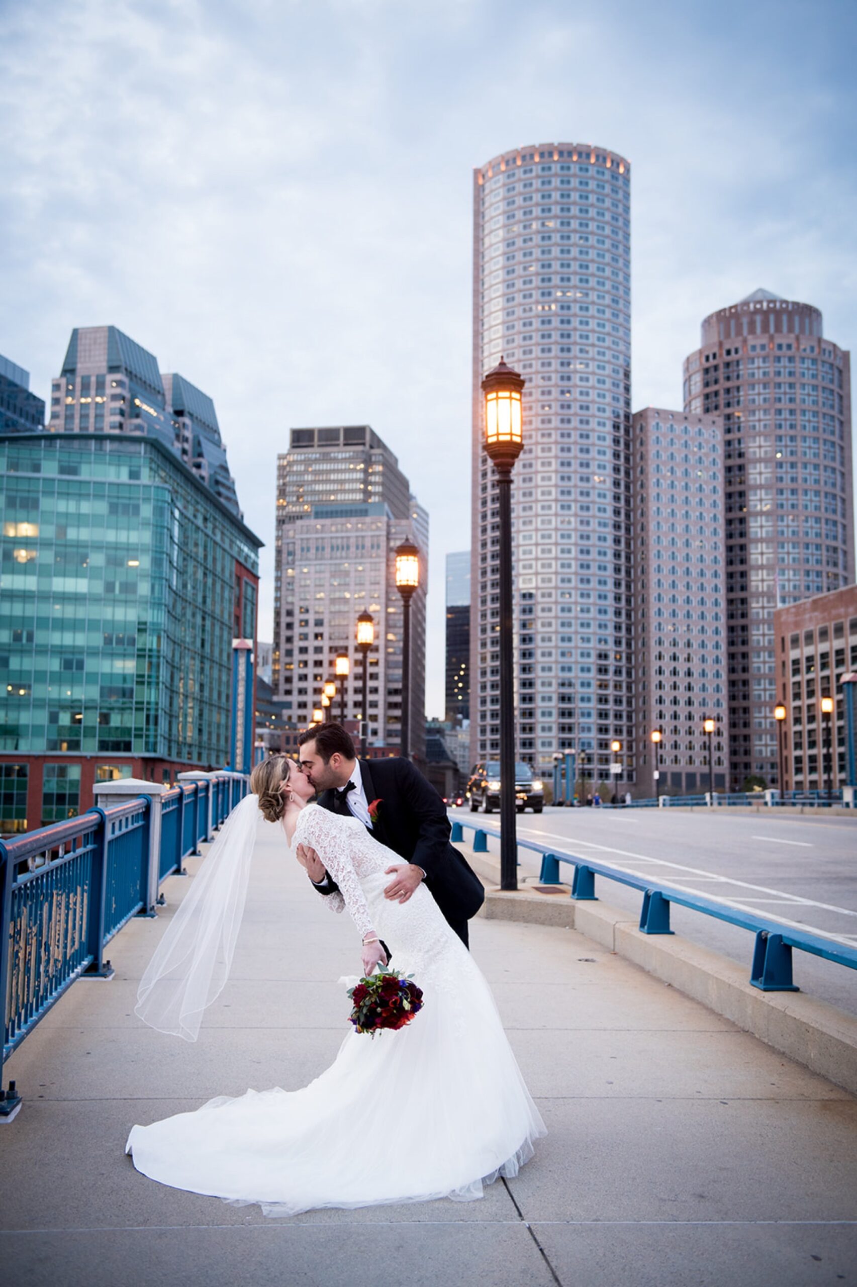 bride and groom kissing on a city bridge with the skyline behind them for their boston Winter Wonderland Wedding