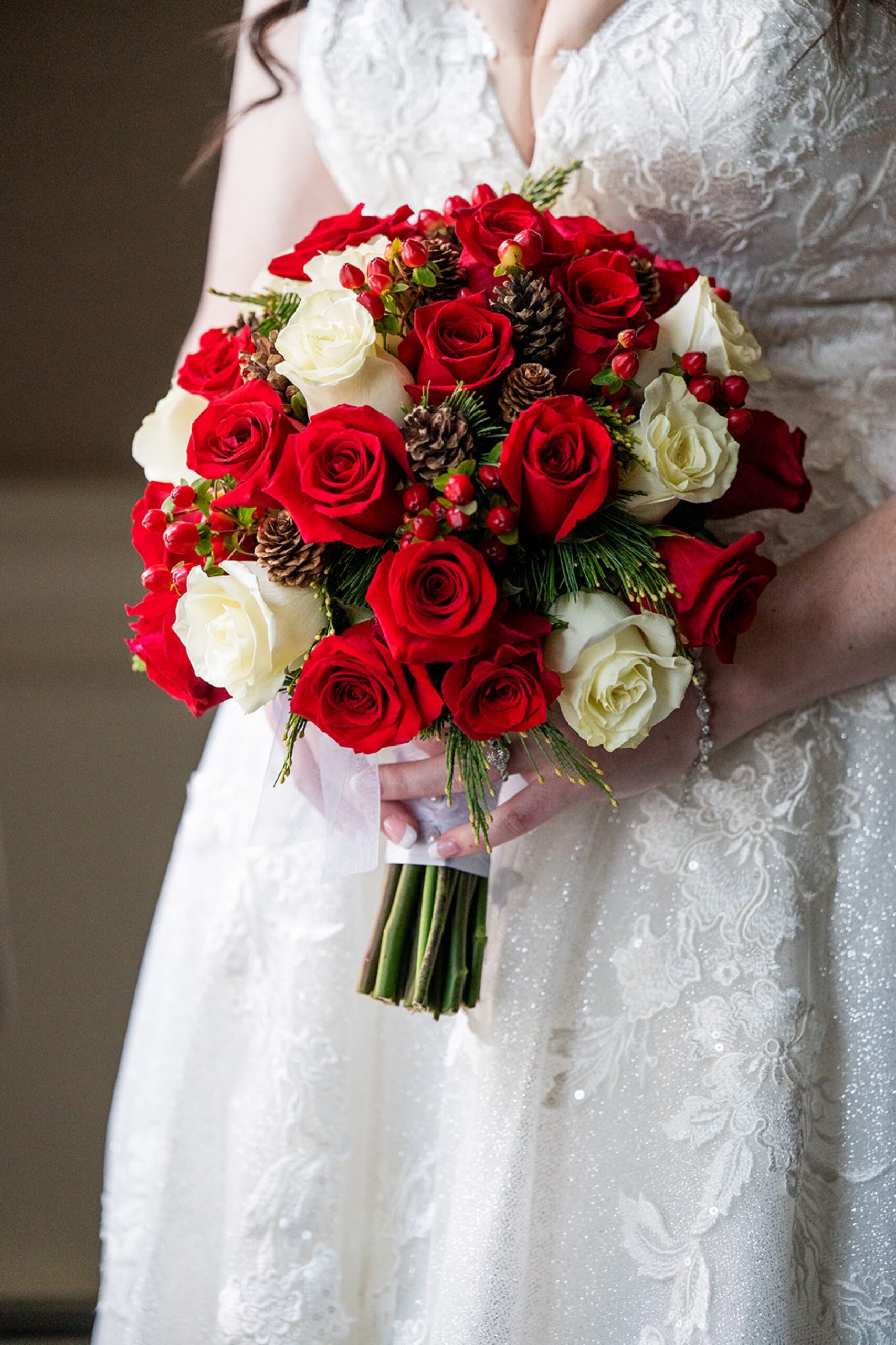 bridal bouquet full of red and white flowers and pine cones tied together with white ribbon 