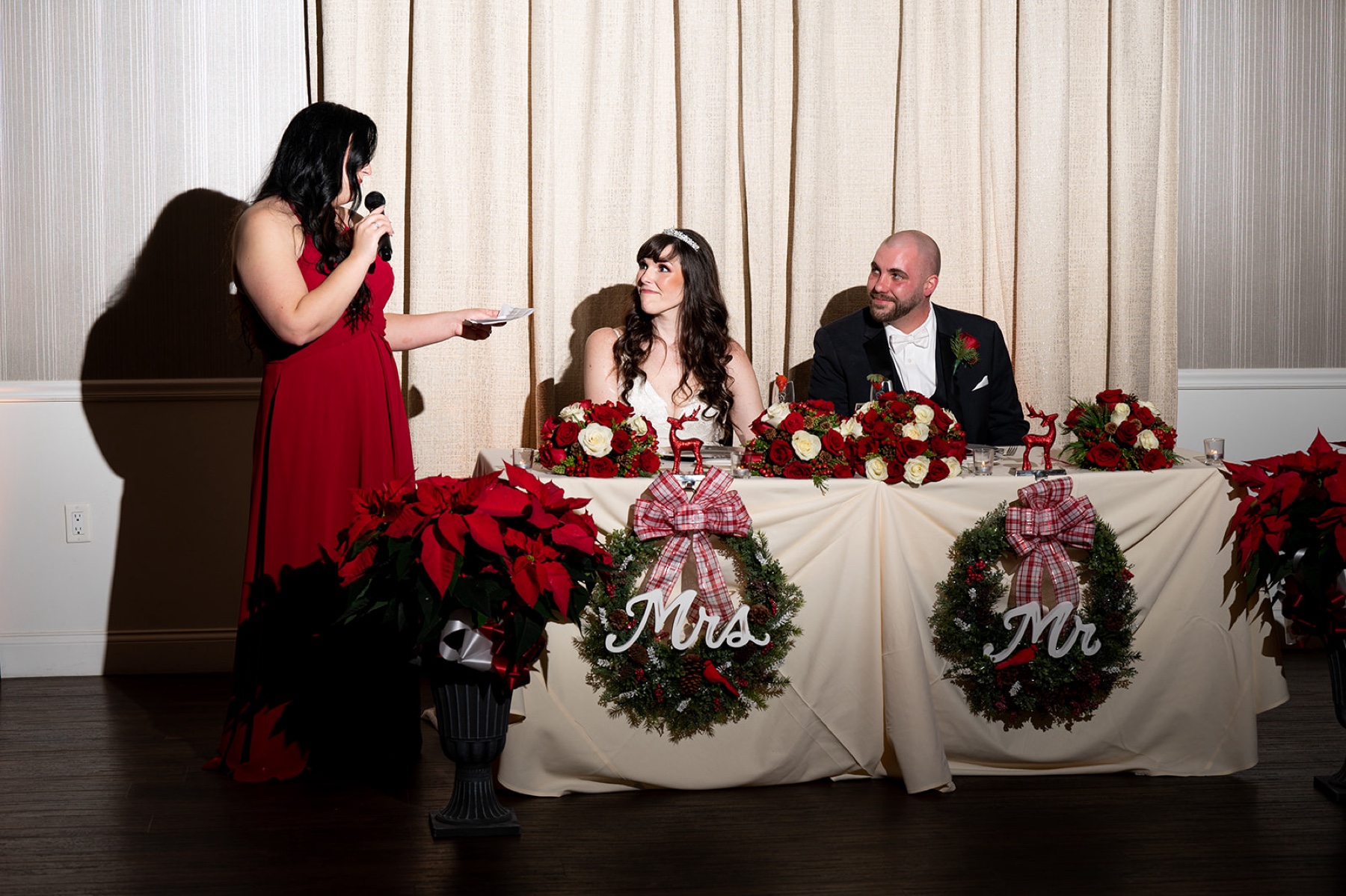 bride and groom listening to bridesmaid give toast in red dress with christmas themed decor surrounding them