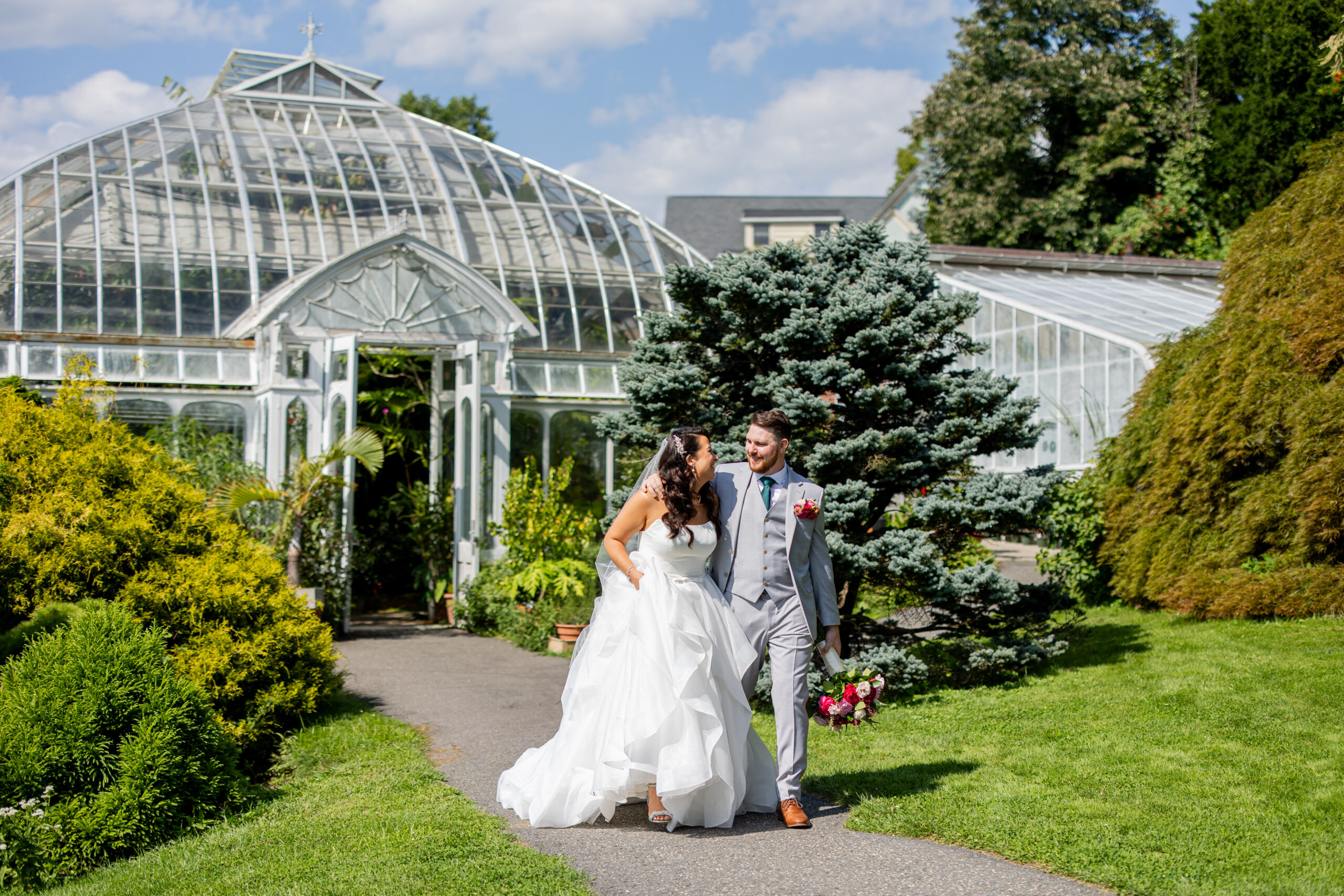 bride and groom walking away from large greenhouse smiling