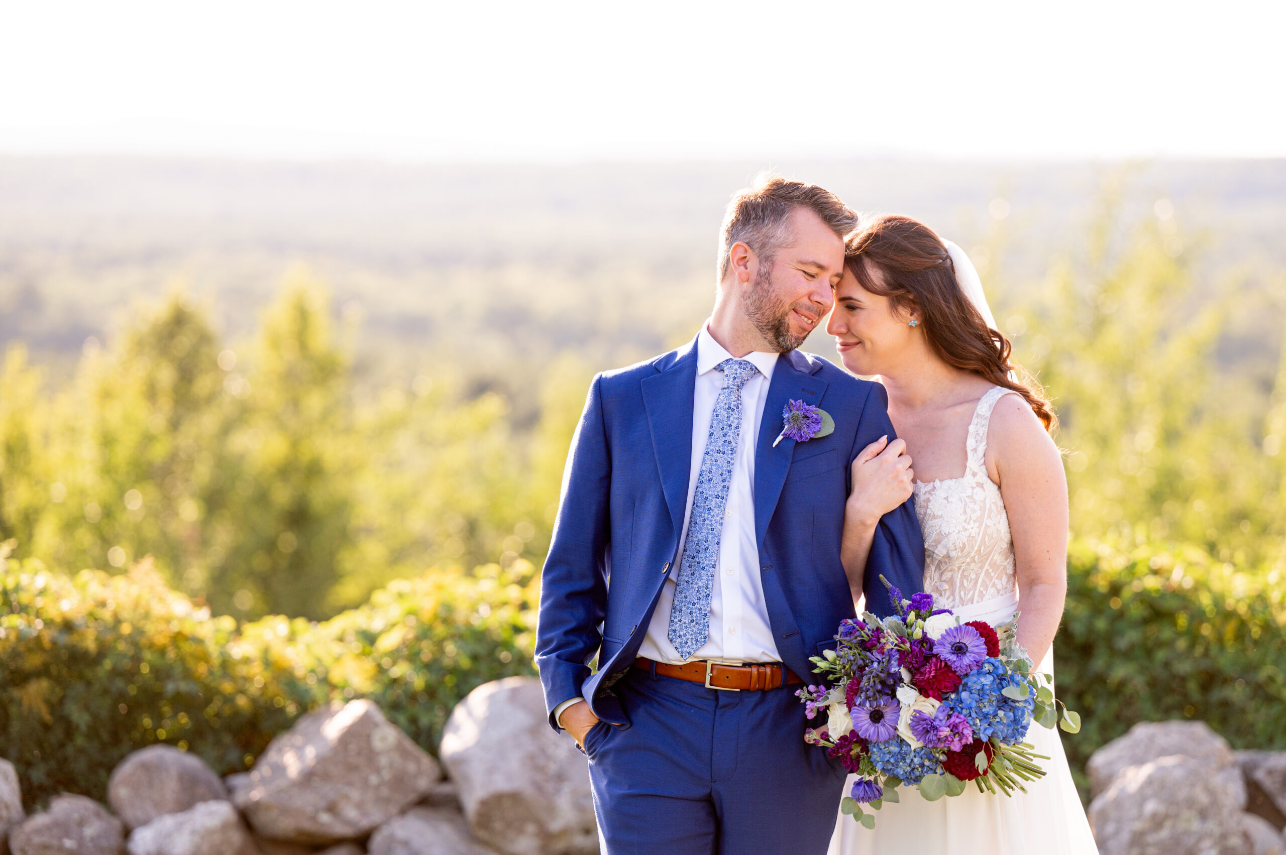 bride holding onto groom's arm and smiling as she carries her purple and blue bouquet 