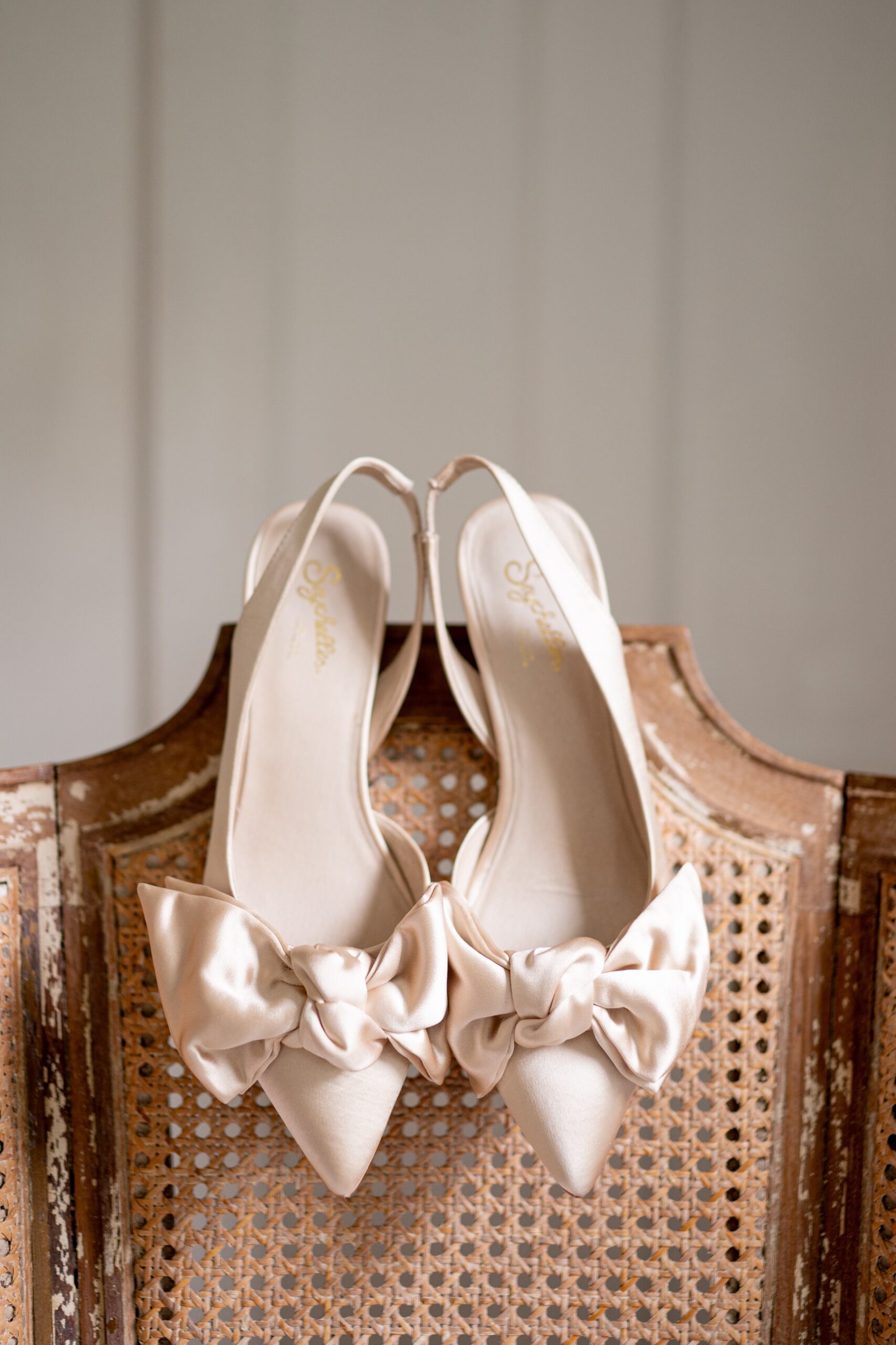 white bridal shoes sitting on the back of a rattan chair