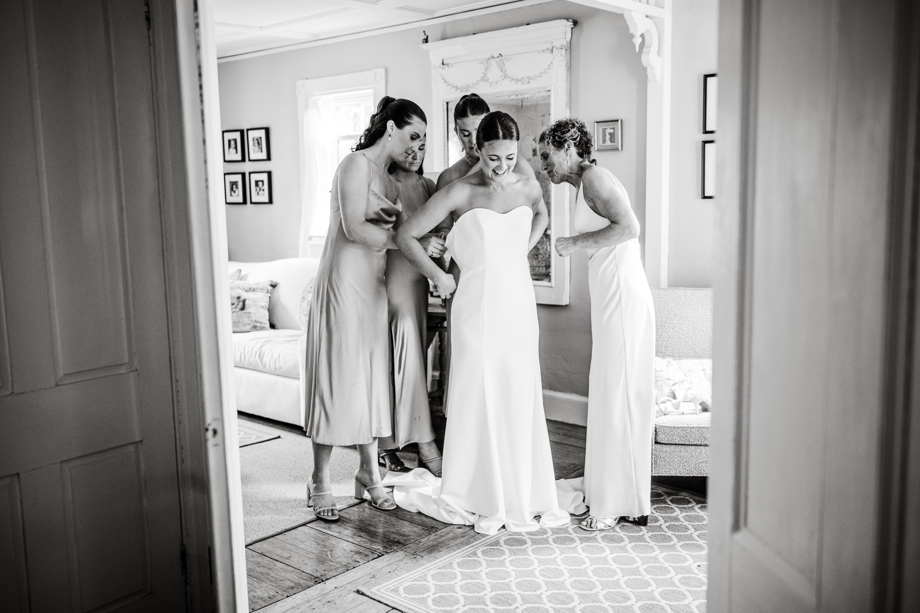 bridesmaids and mother of the bride helping her into the wedding dress 