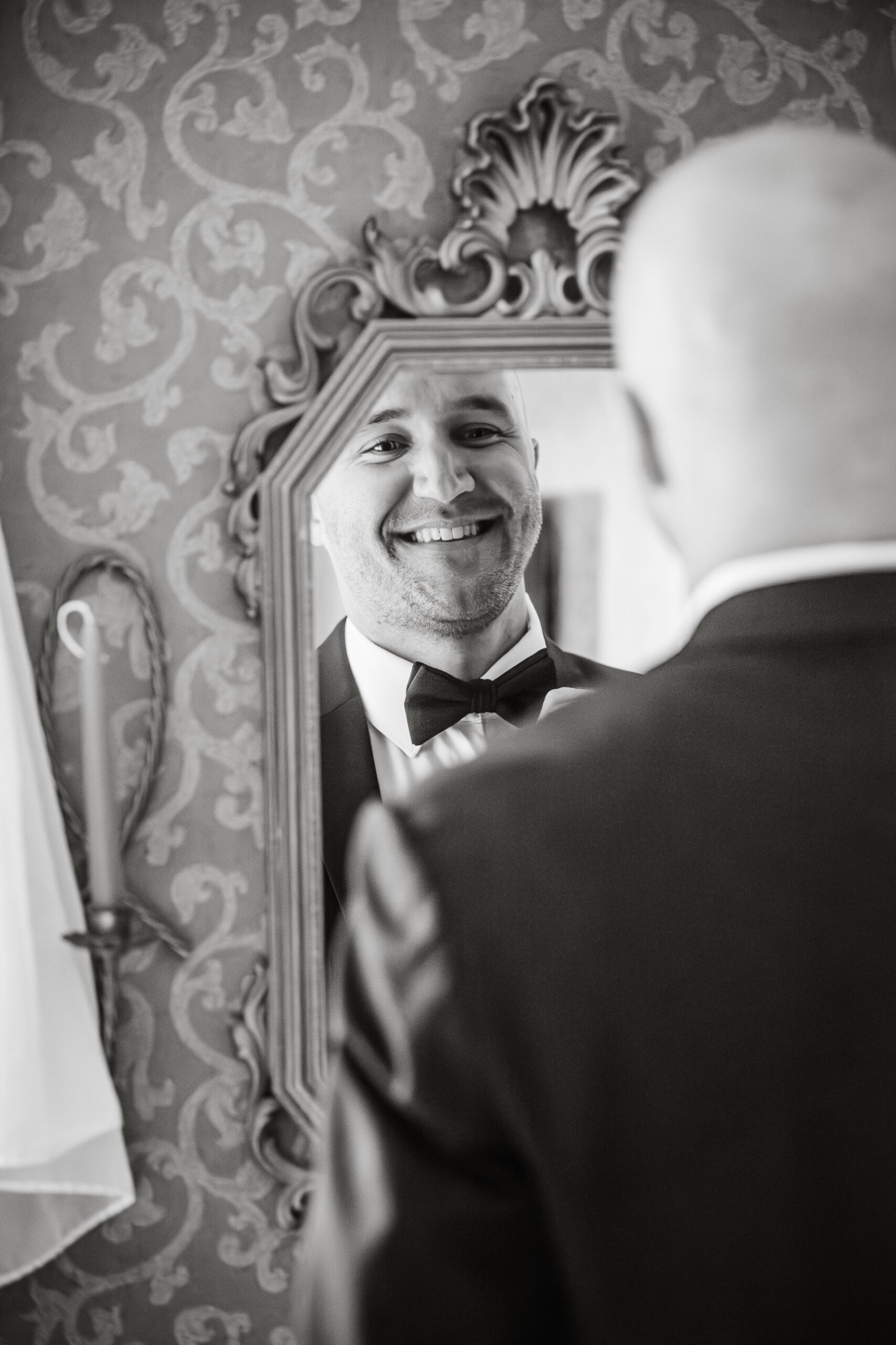 groom smiling at himself in the mirror as hr ties his bowtie 