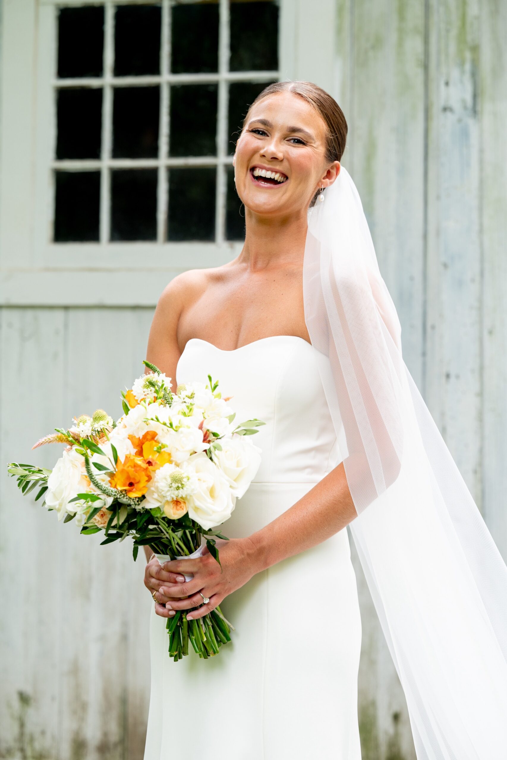 bride laughing at the camera holding her white and orange floral wedding bouquet 