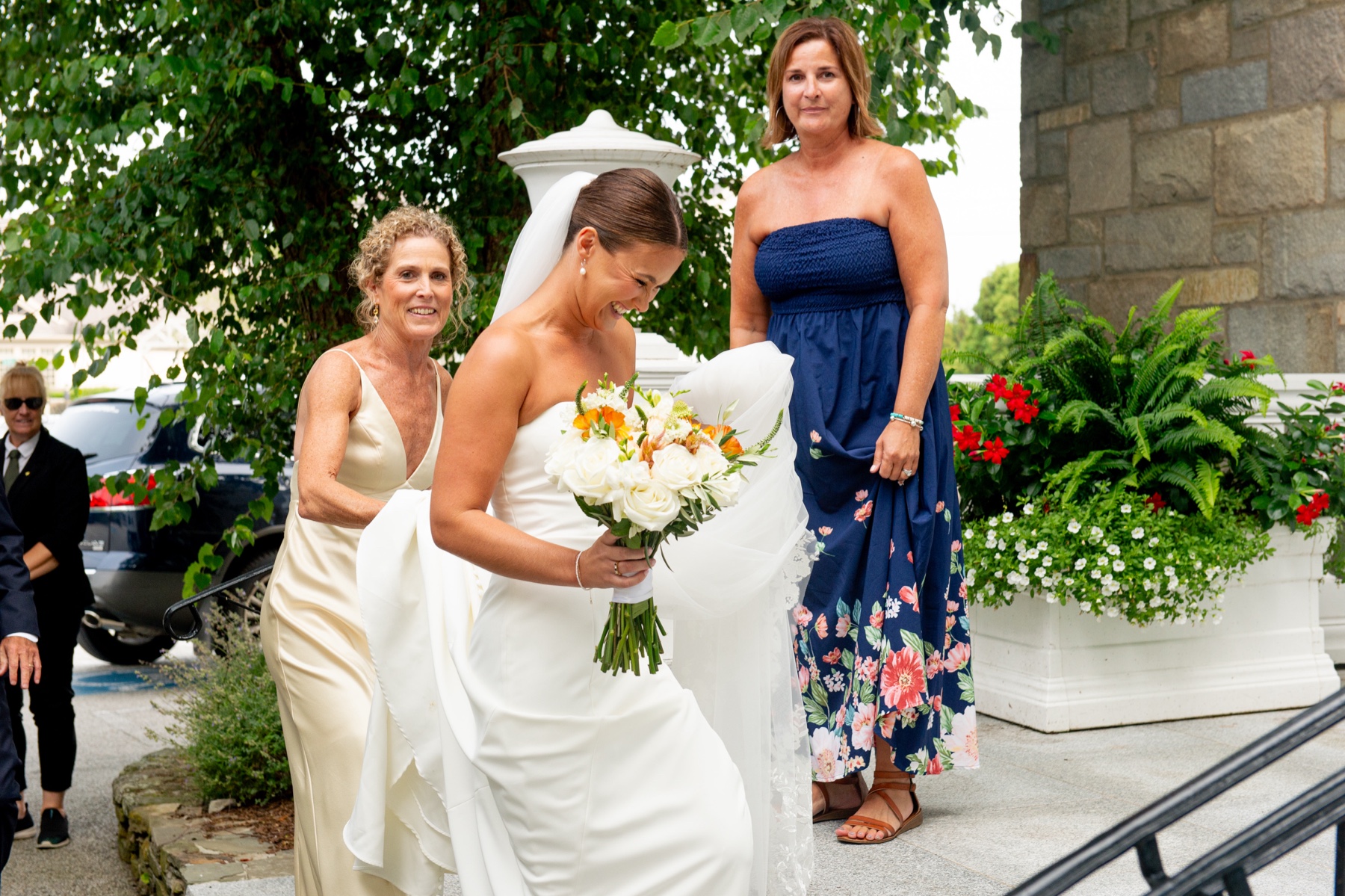 bride walking up the steps of the South Shore church as her mother holds her train and veil behind her 