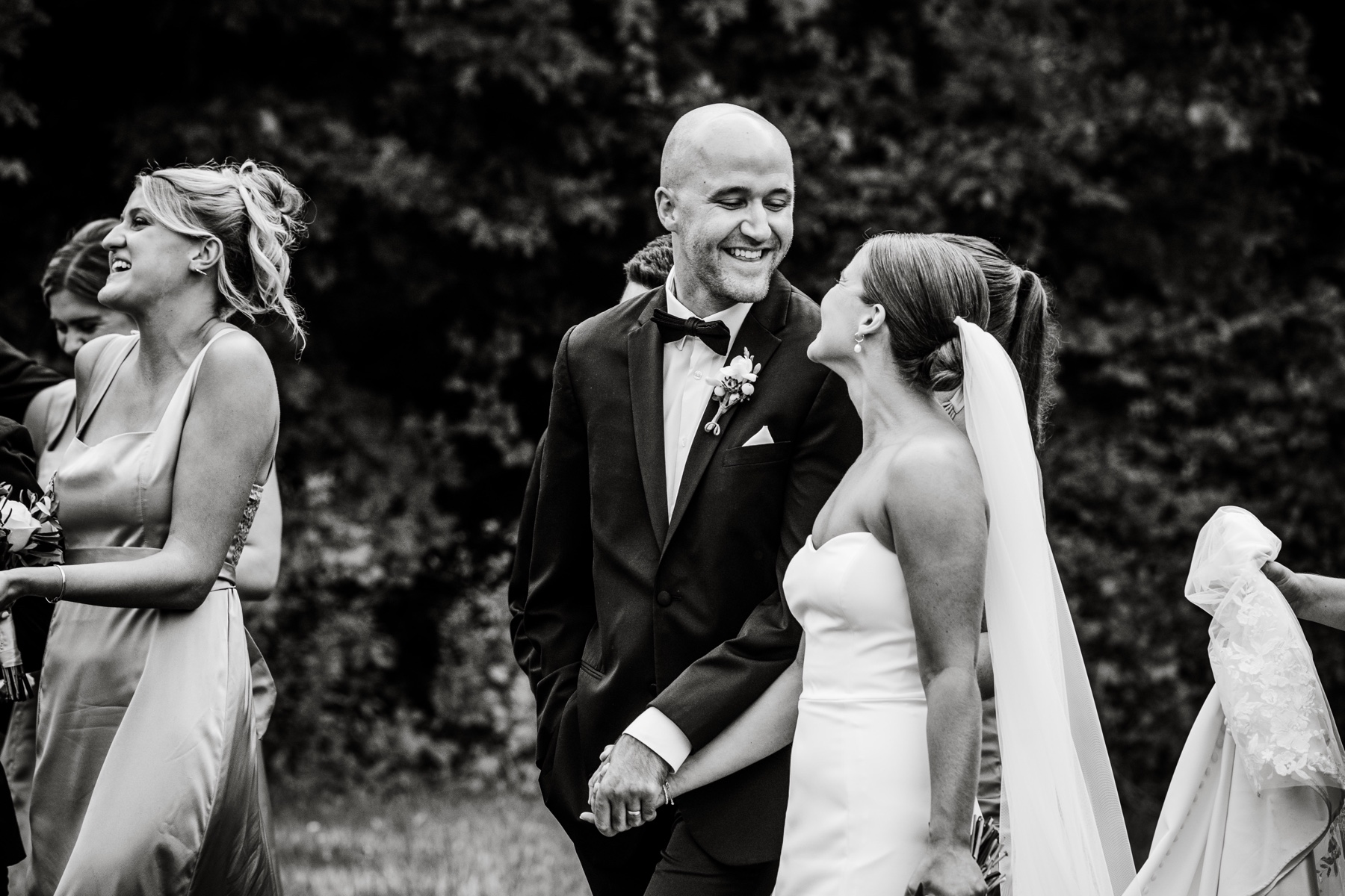 bride and groom smile at each other as they walk along with the bridal party 