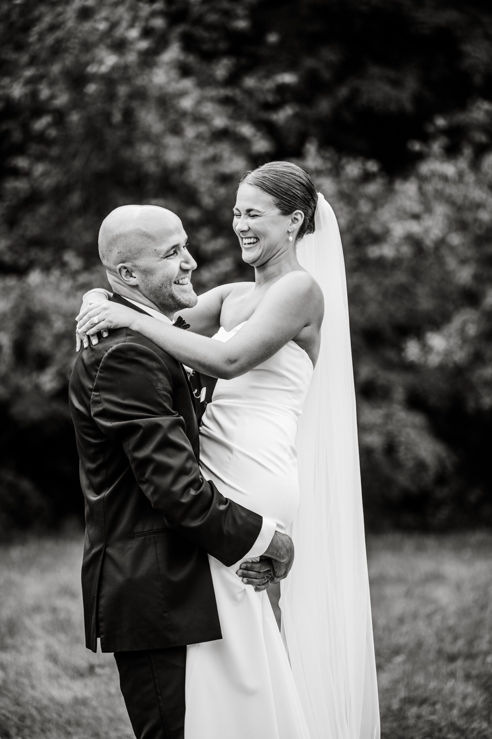 bride laughing as the groom picks her up for a photo