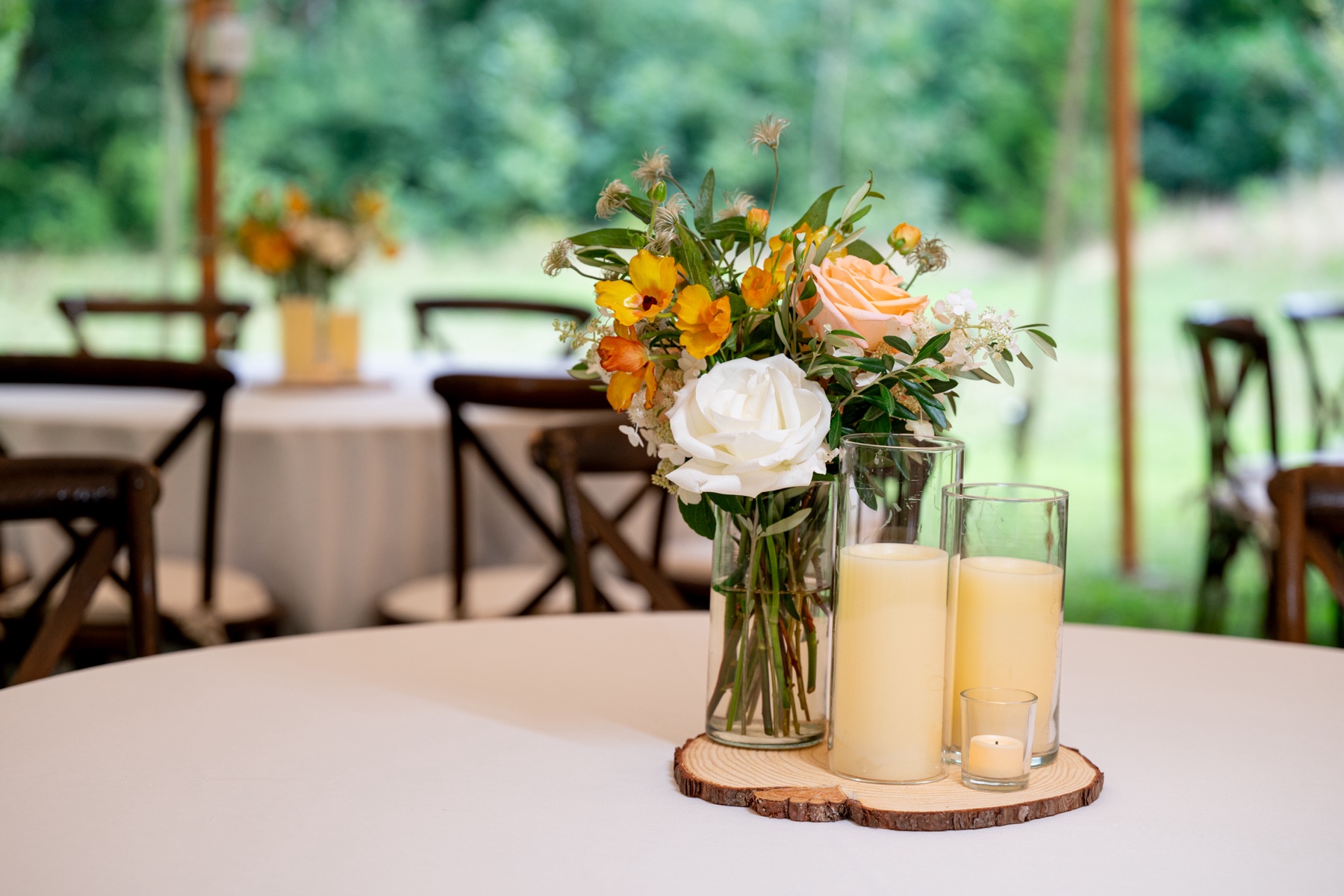 orange and white floral centerpiece sitting next to white candles on top of wooden bark platter at wedding reception 