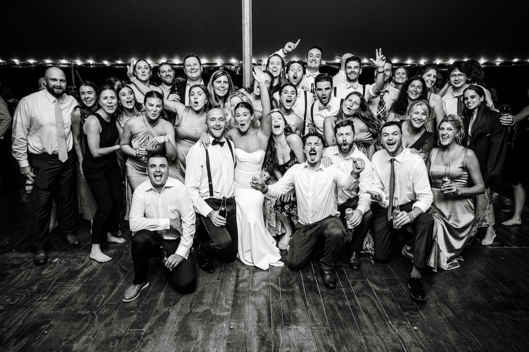 bride and groom pose on the dance floor for a group picture with wedding guests 