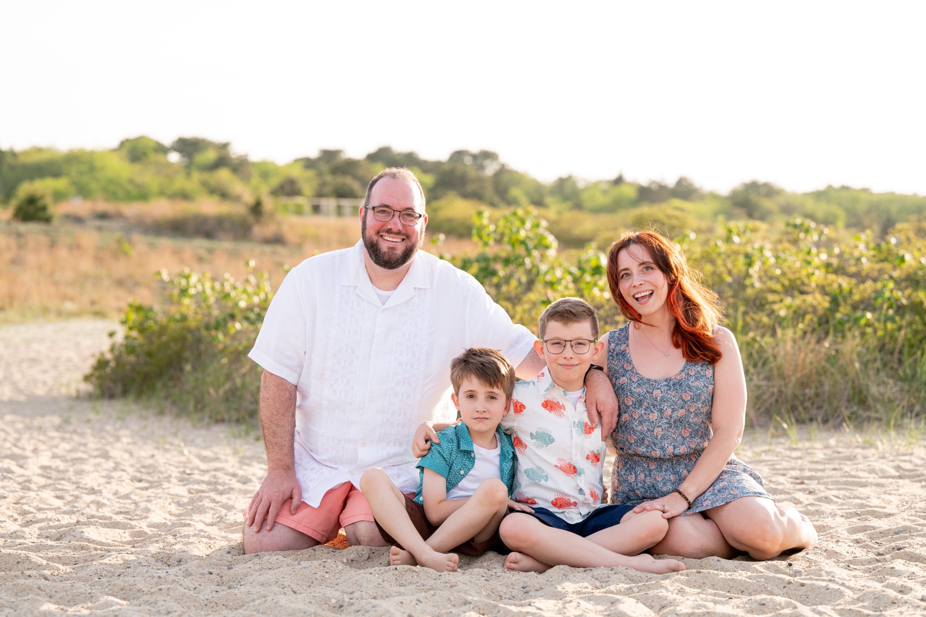 a father and mother and their two sons sitting on the sandy beach