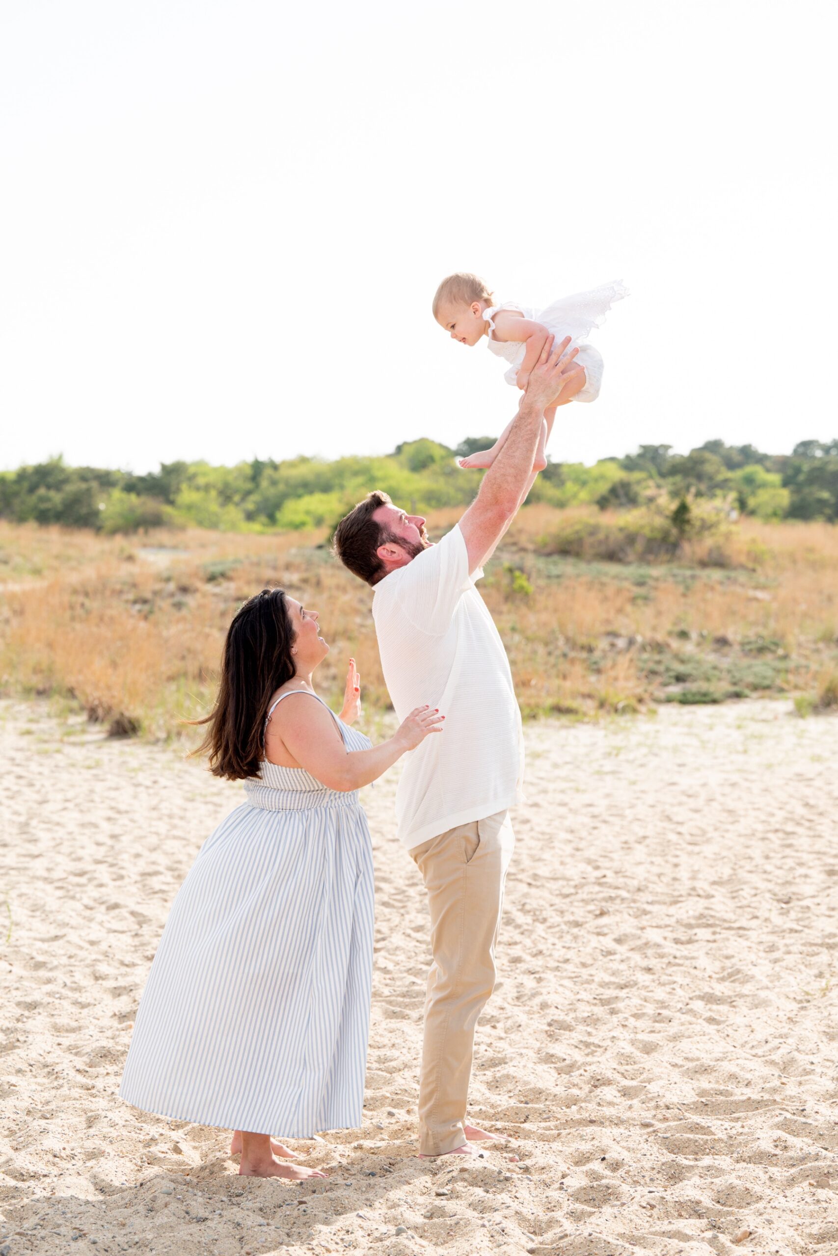 father throws his baby daughter gently in the air at the beach with the mother standing next to him