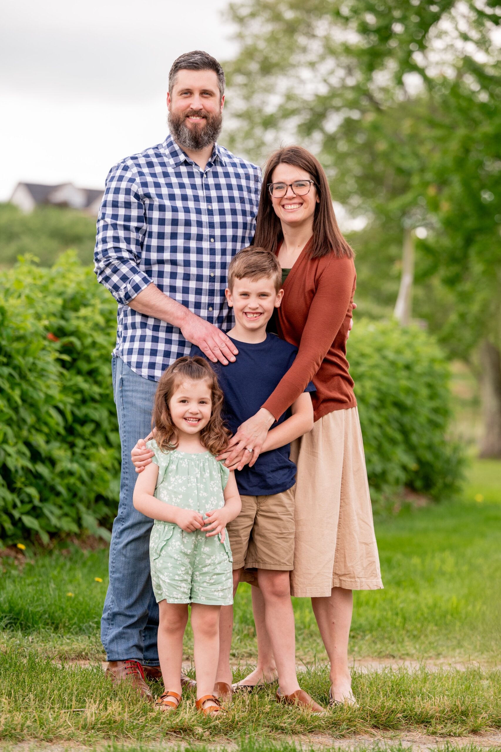 family of four standing in grassy apple orchard for their spring family portrait