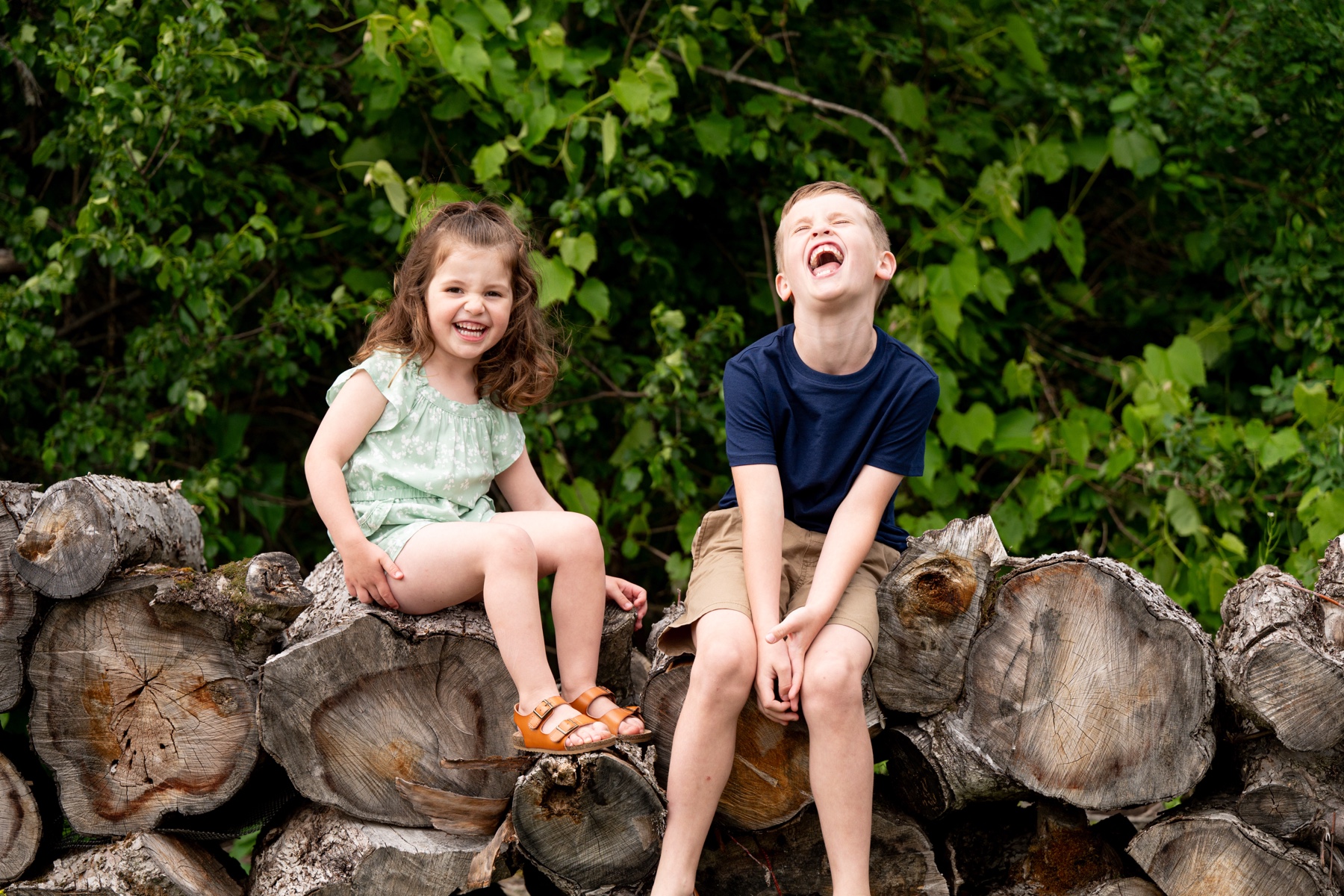 young boy and girl sitting on a pile of logs smiling