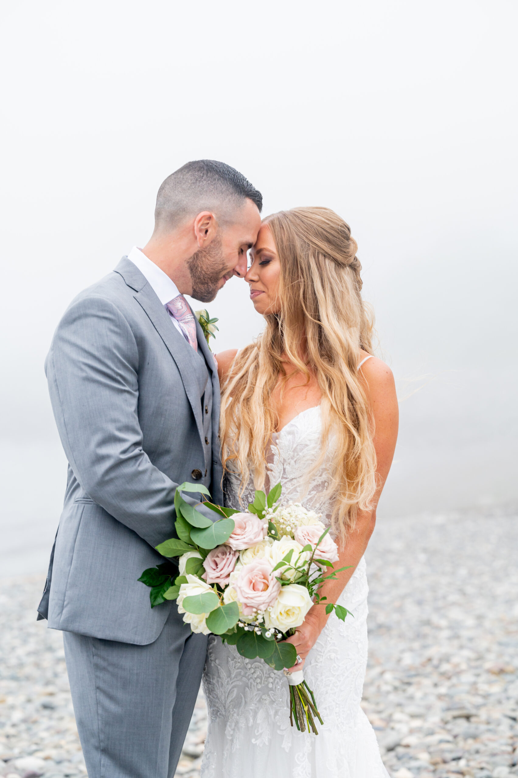bride and groom embracing with foggy background by the ocean on a rainy day wedding