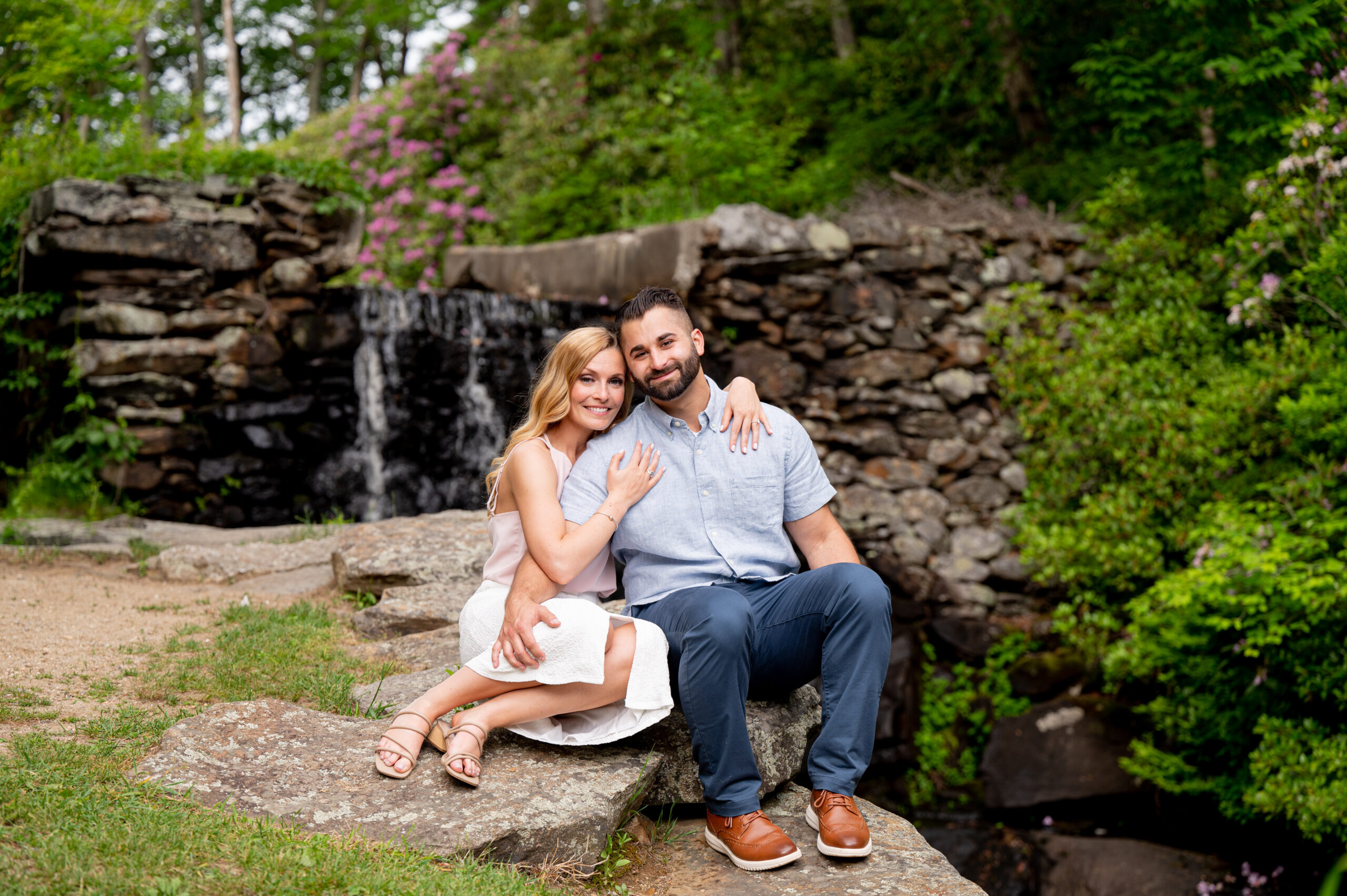 couple sitting on rocks in a park with waterfall behind them