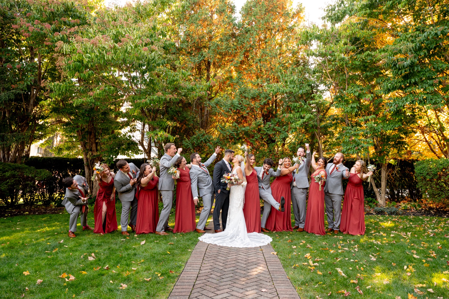 bride and groom posing with their wedding party with red dresses and grey suits