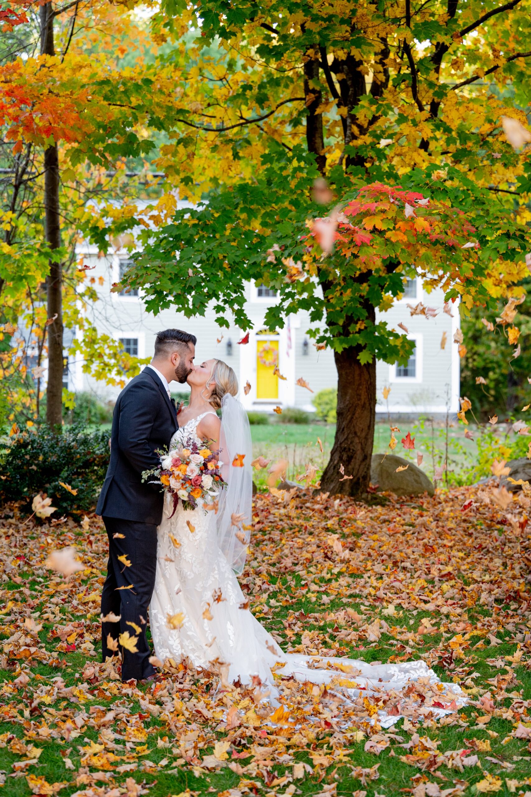 bride and groom kissing surrounded by fall leaves and trees in New England