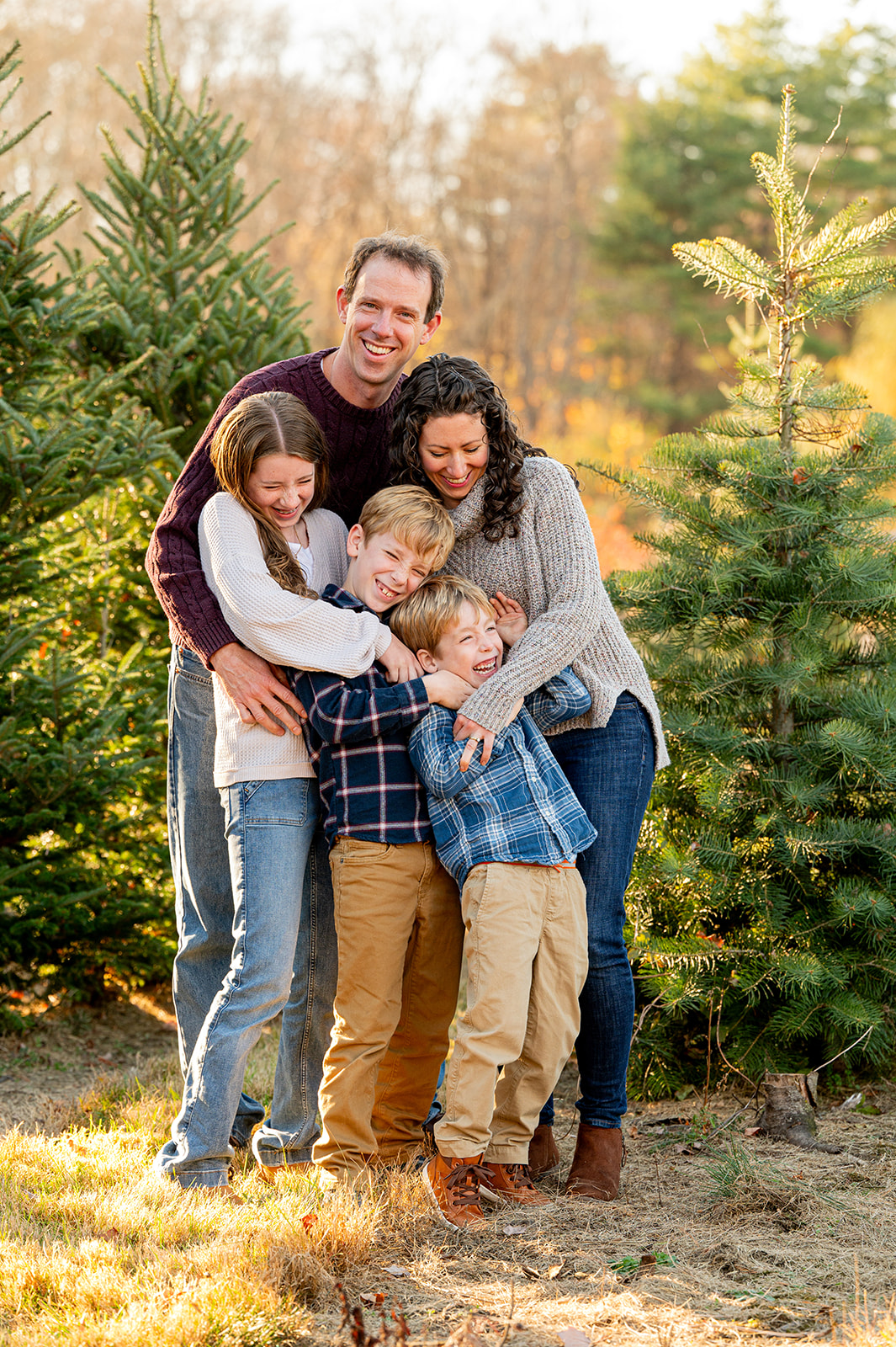 family of five hugging in a christmas tree farm