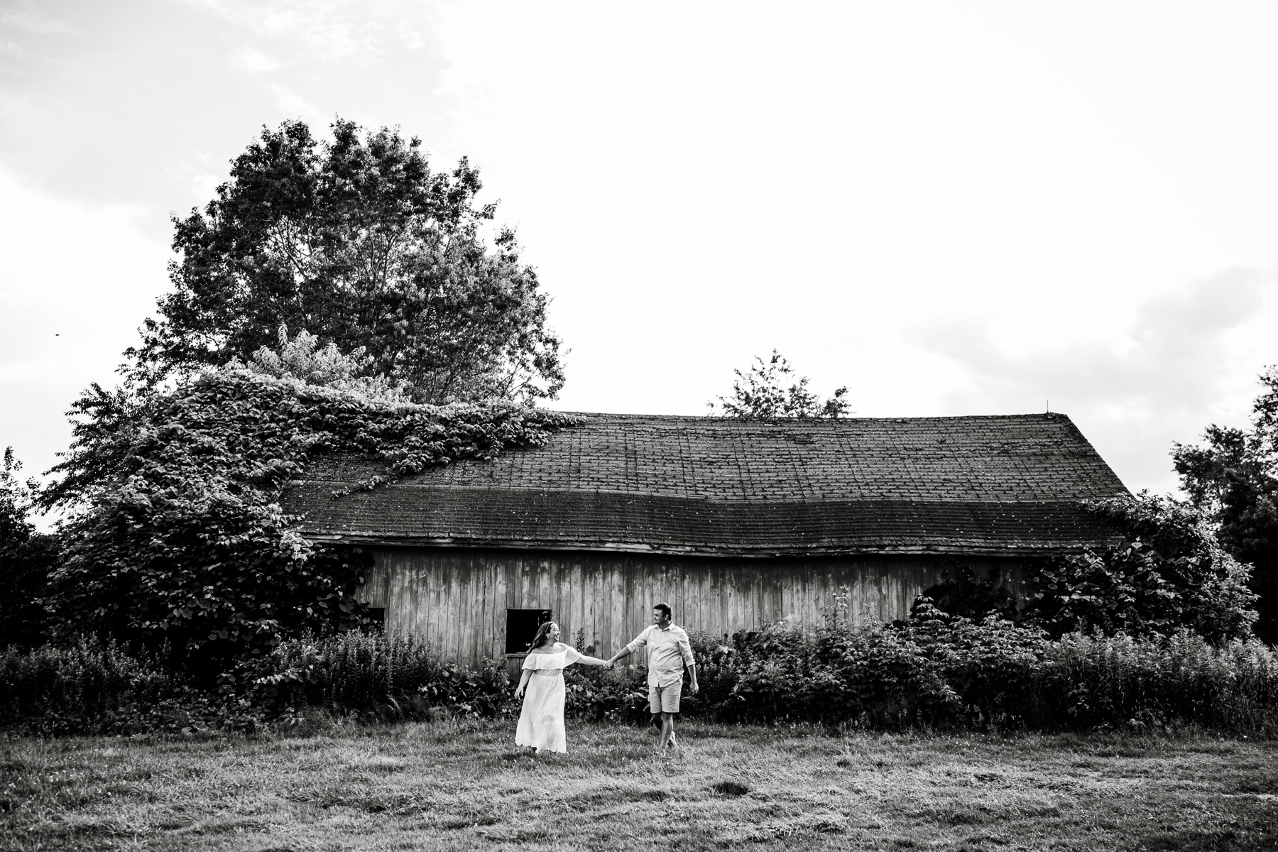 couple holding hands and walking in front of an old barn at the shaw farm in sutton ma 