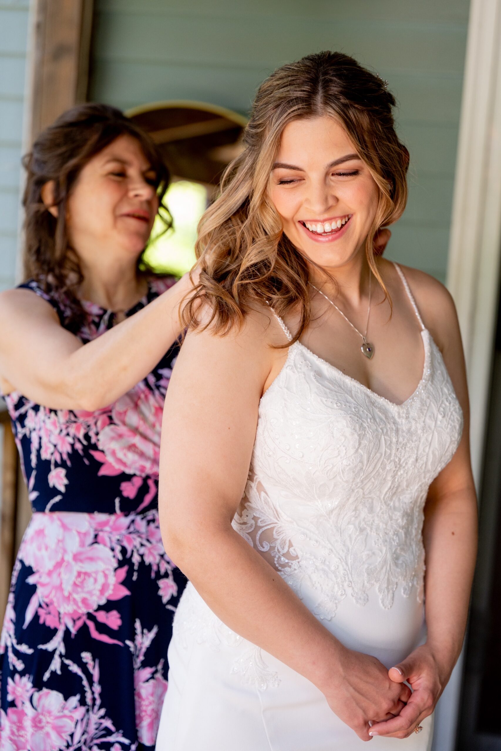 the bride smiling as her family member buttons the back of her dress 