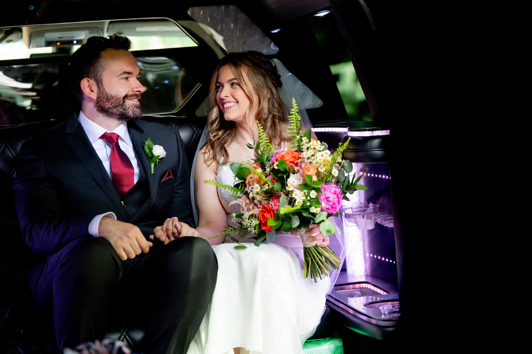 bride & groom sitting in the back of a limo holding a brightly colored bouquet