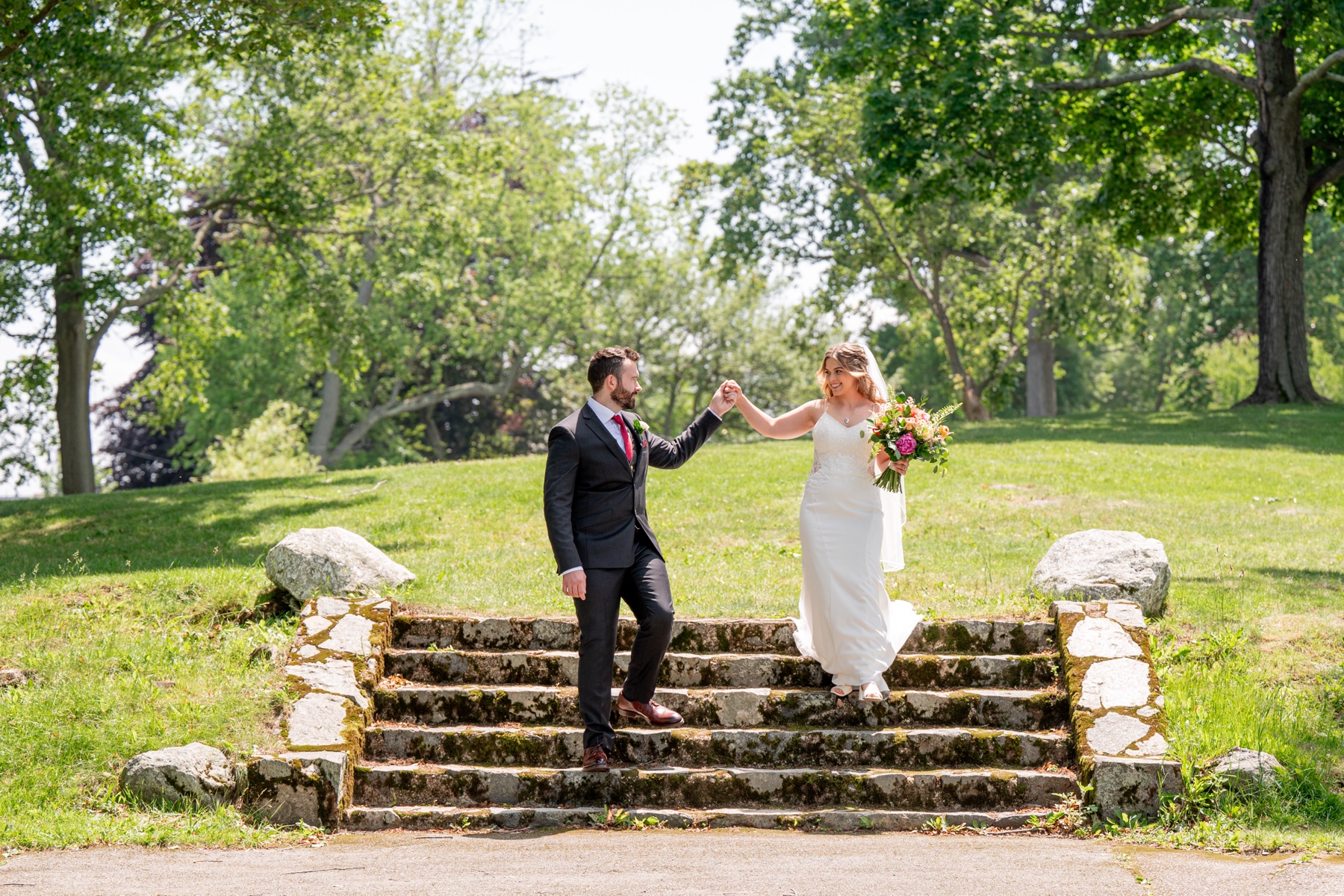 bride and groom holding hands as they walk done stone steps in a park