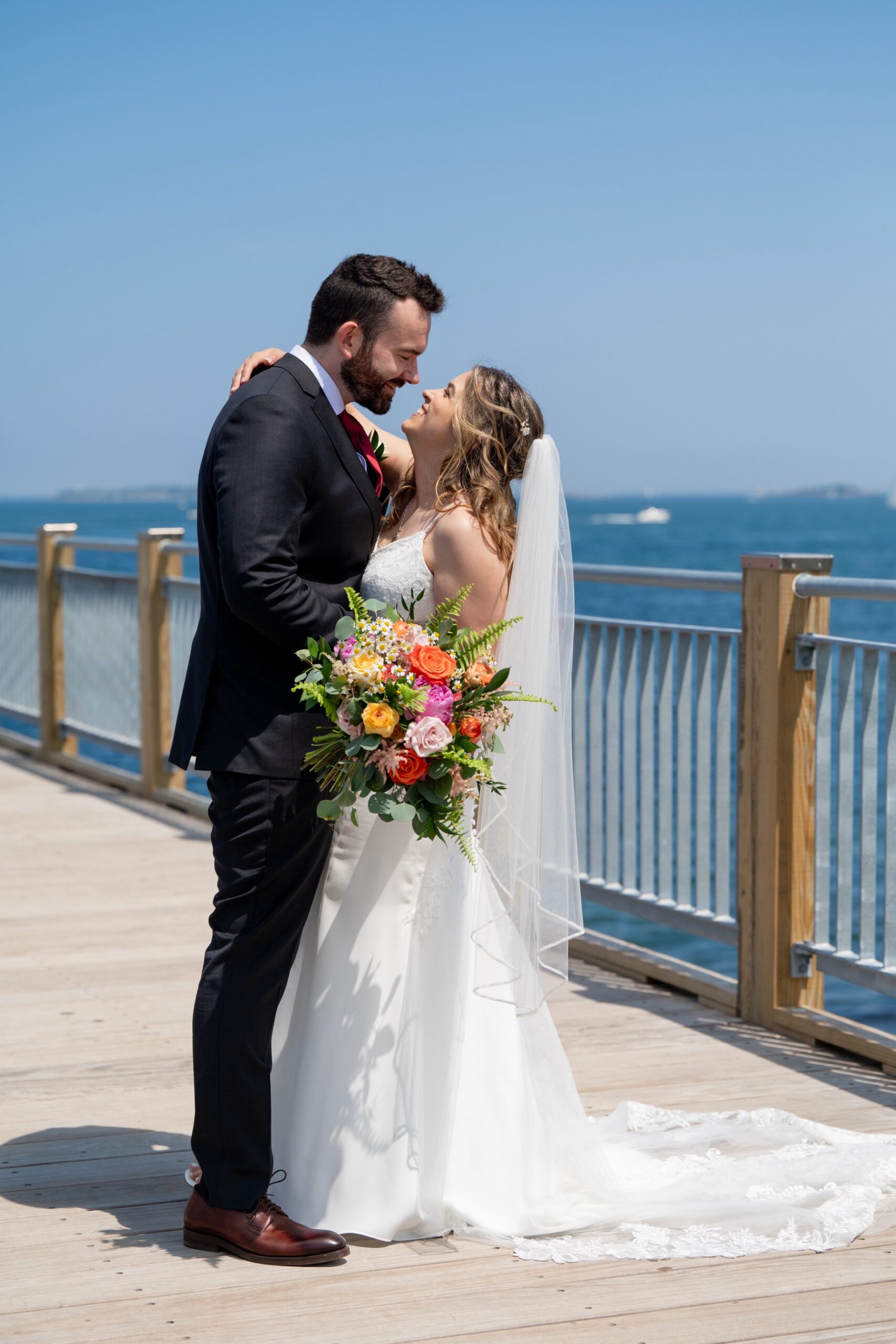 bride and groom embracing on the pier surrounded by blue water