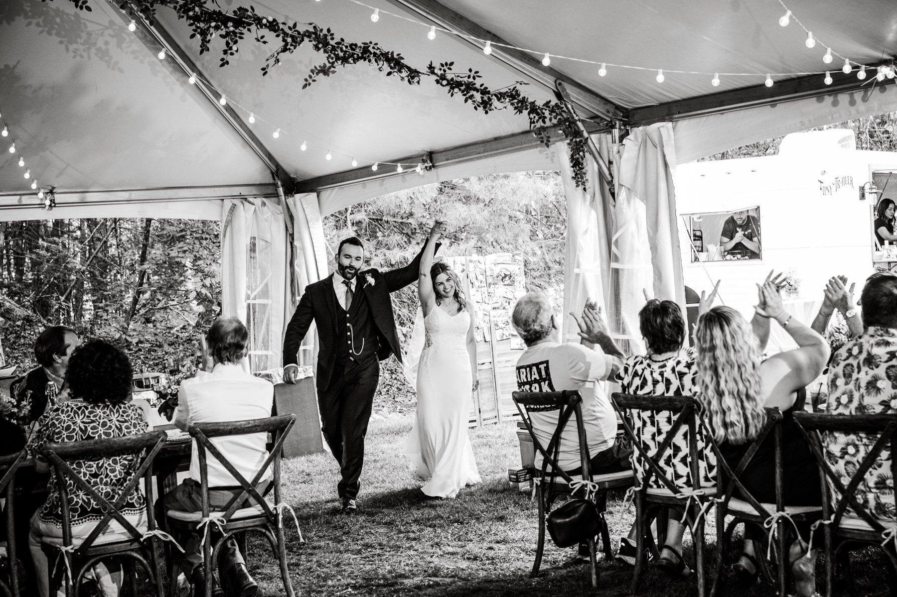 bride and groom entering the tent for their wedding reception with guests clapping 